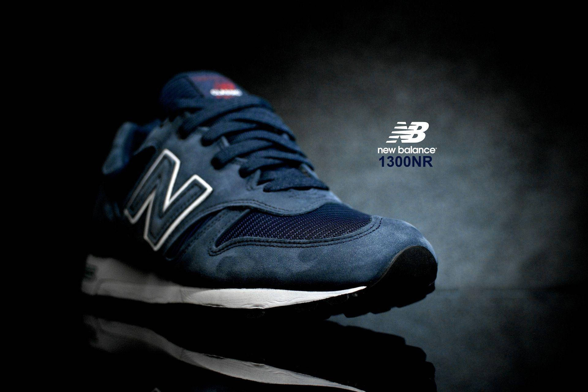 驚艷新百倫深藍色運動鞋 壁紙 — 時尚的深藍色 New Balance 1300NR 運動鞋在戲劇性的聚光燈下，在帶有反射表面的煙霧黑色背景上發光。