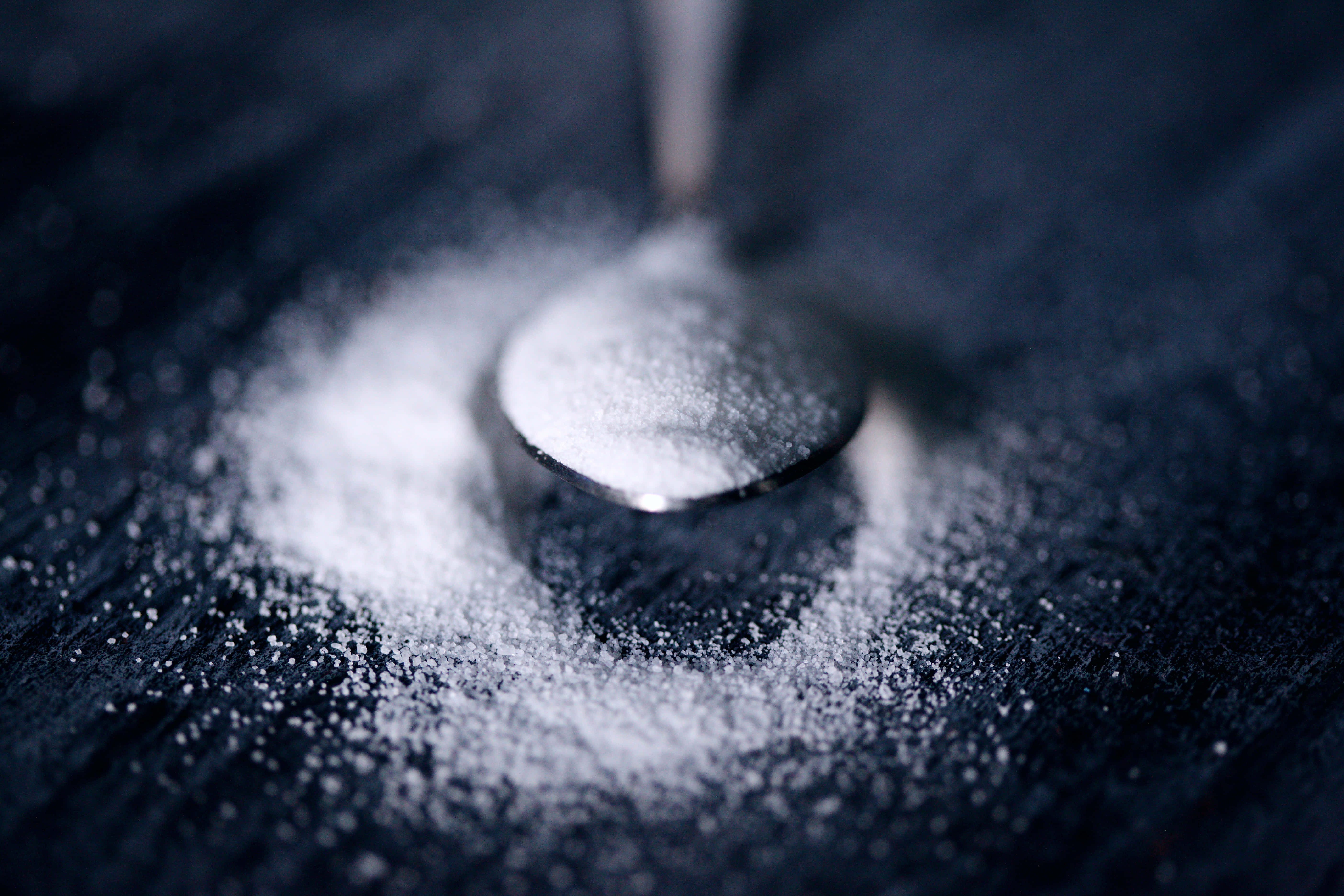 驚艷銀色茶匙 壁紙 — 特寫鏡頭：砂糖從湯匙灑落在深色紋理表面上，景深較淺。