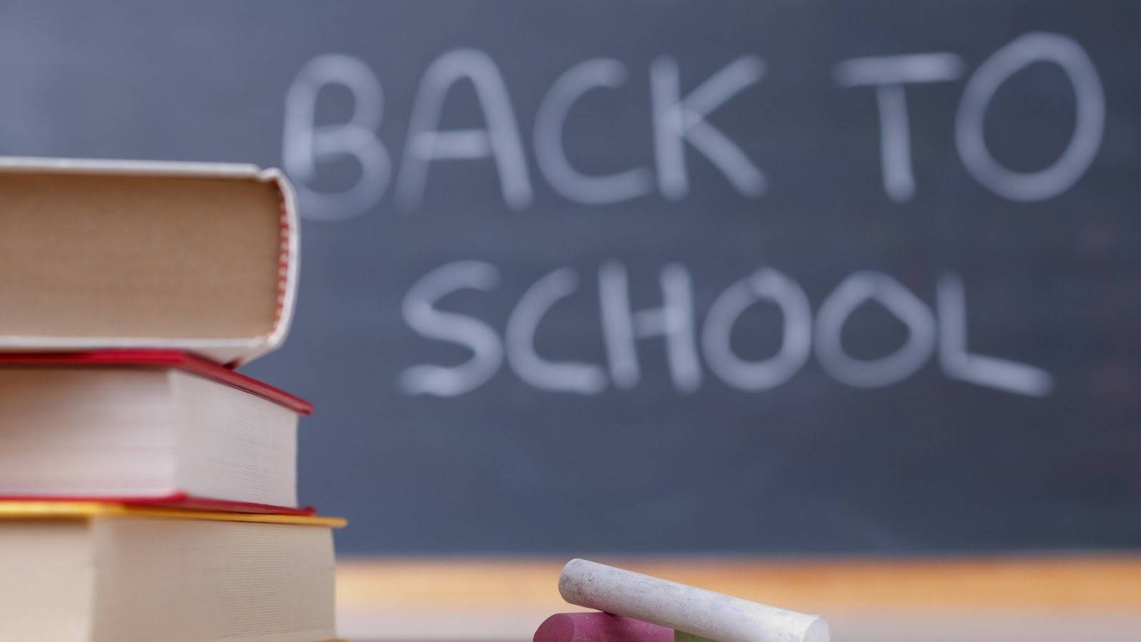 一堆書本和粉筆放在黑板前，黑板上寫著 back to school。