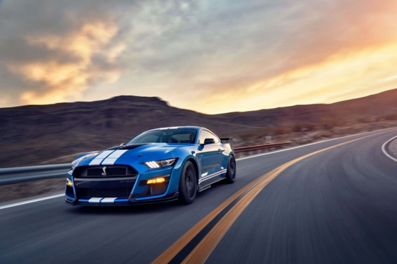 藍色 Shelby Mustang GT500 在日落時分在沙漠高速公路上疾馳。
