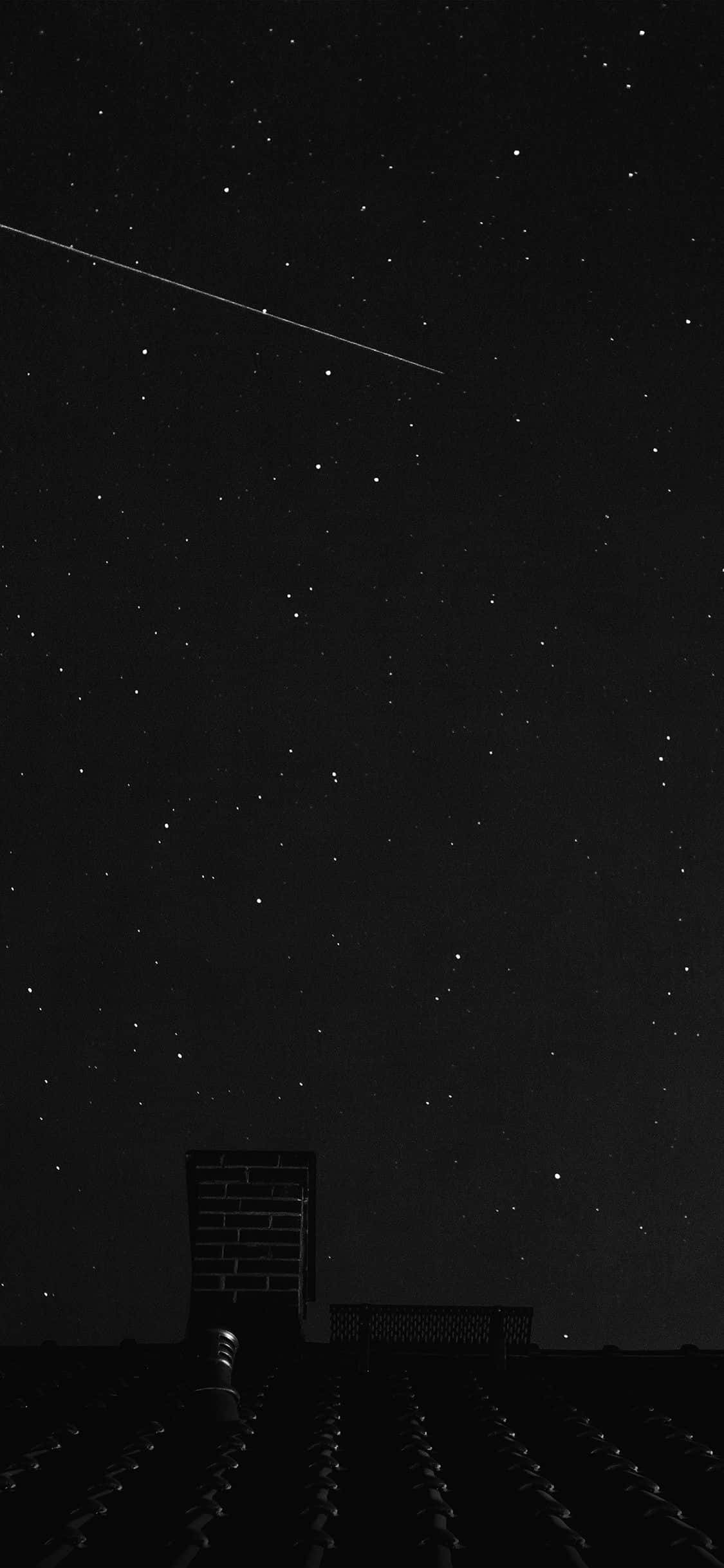 體驗 Apple iPhone 11 Pro 美觀黑色版的強大性能 壁紙 — 繁星點點的夜空，一顆明亮的流星劃過黑暗的屋頂煙囪上方。