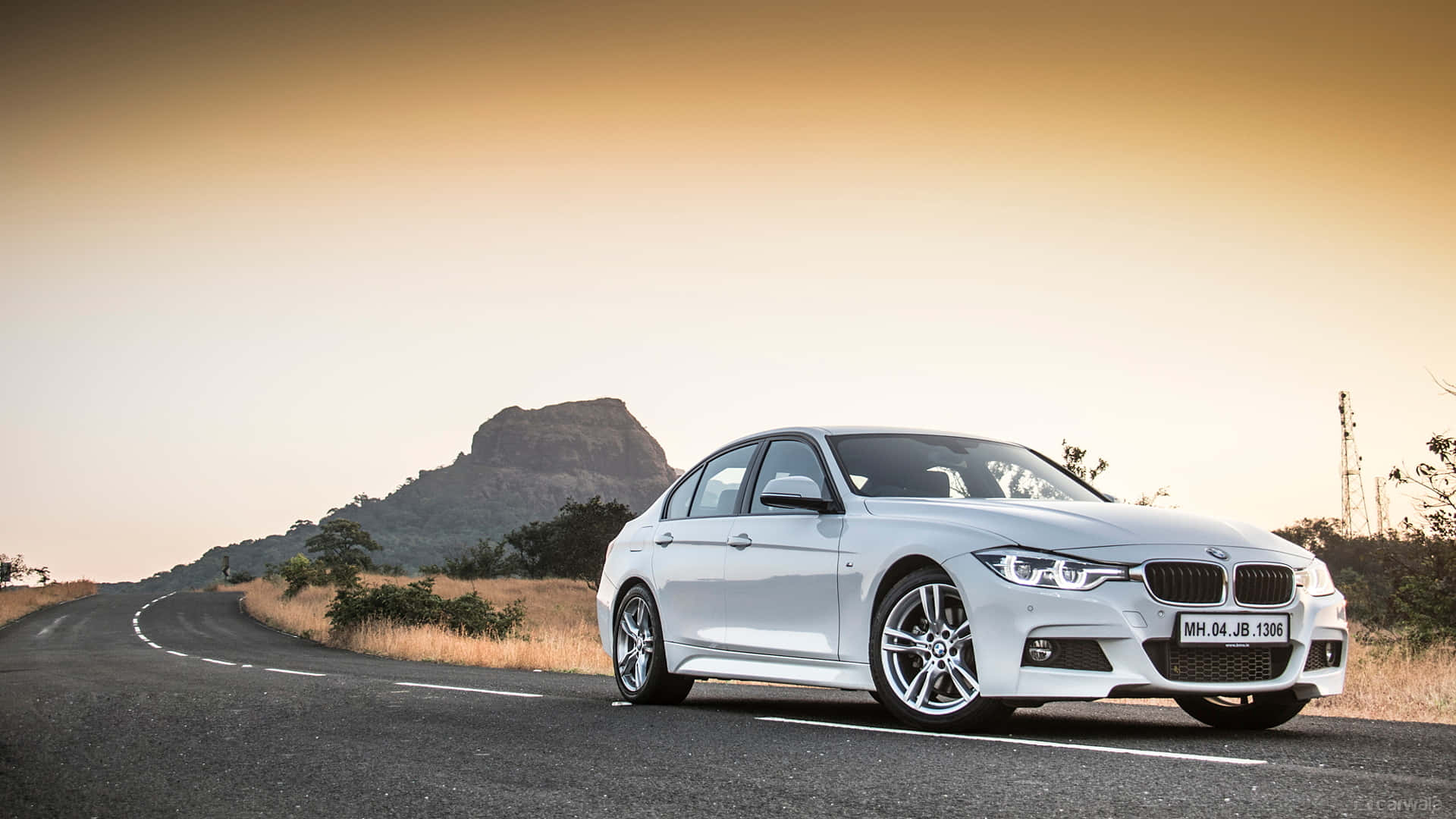 金色夕陽下，白色BMW房車在蜿蜒的山路上。