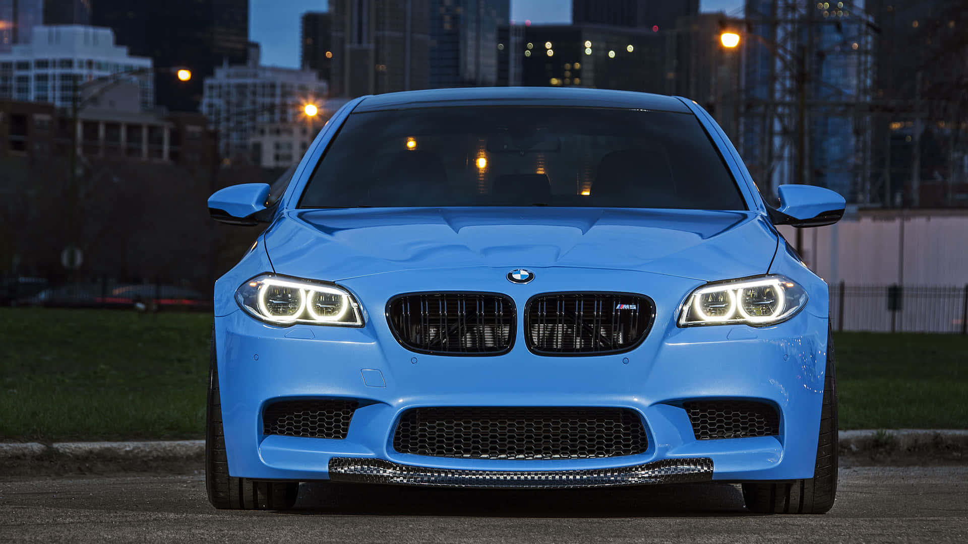 藍色BMW M5夜間停泊在城市中，車頭燈亮起。