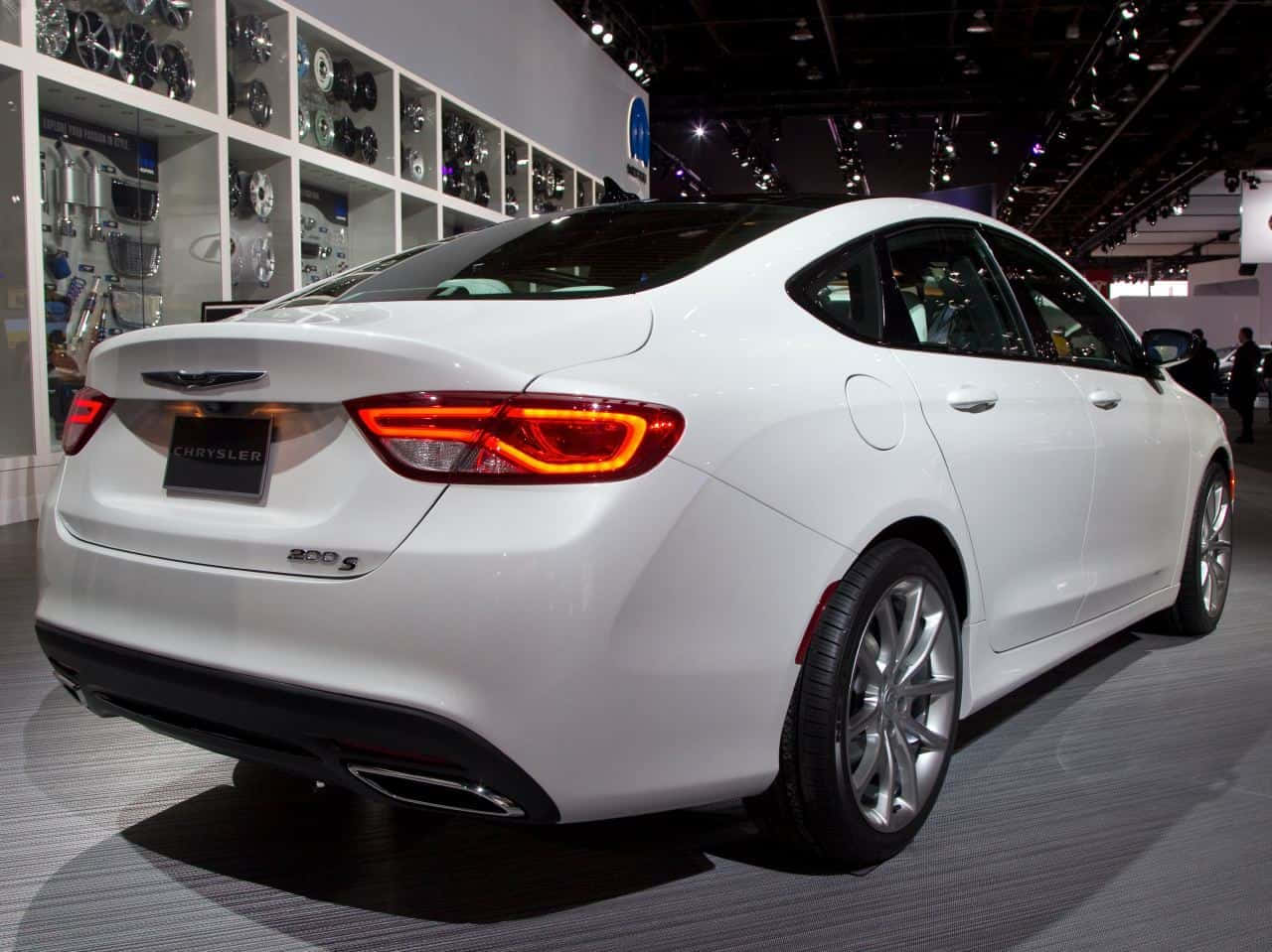 體驗 Chrysler 的奢華駕馭感 壁紙 — 一輛時尚的白色 Chrysler 200S 轎車在車展上展出，配備發光的尾燈和鍍鉻輪圈，在明亮的展覽燈光下。