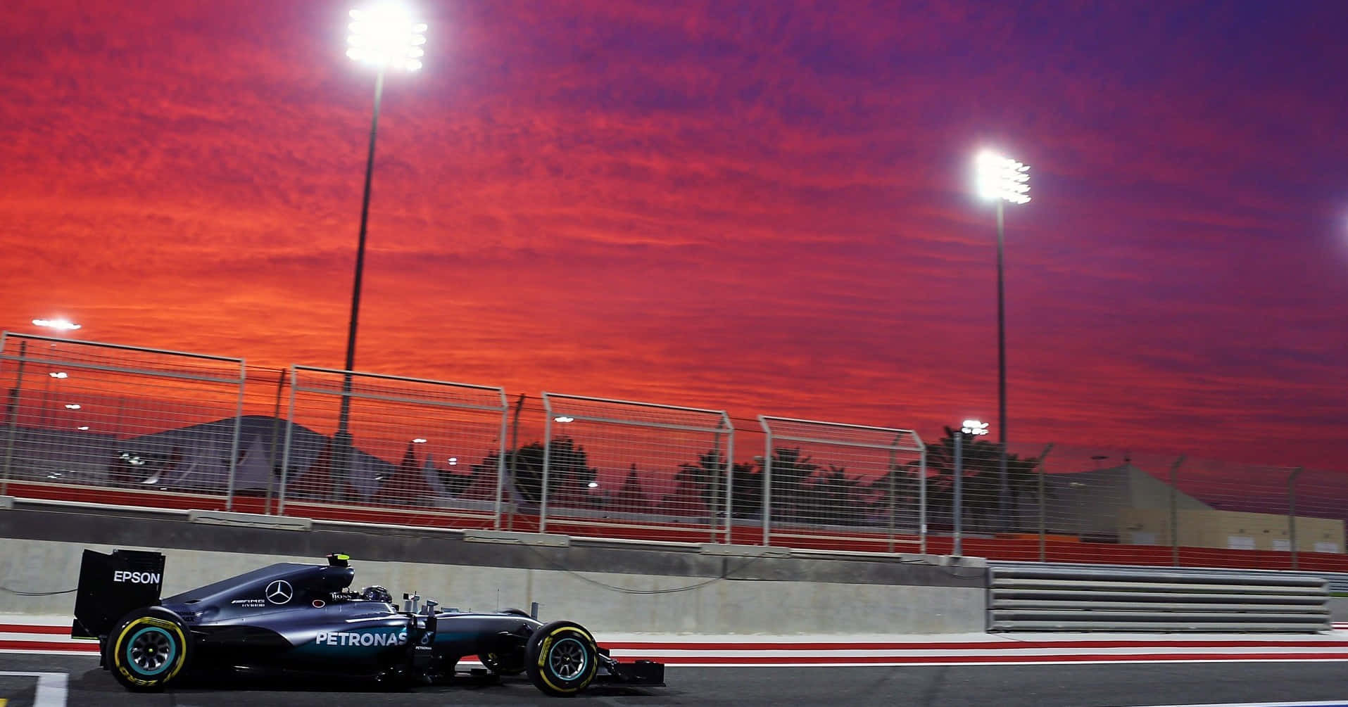 體驗 F1 賽車的驚險刺激 — F1 2016 壁紙 — 一輛梅賽德斯一級方程式賽車在戲劇性的紅色和紫色夕陽天空下，在體育場燈光照亮的賽道上奔馳。