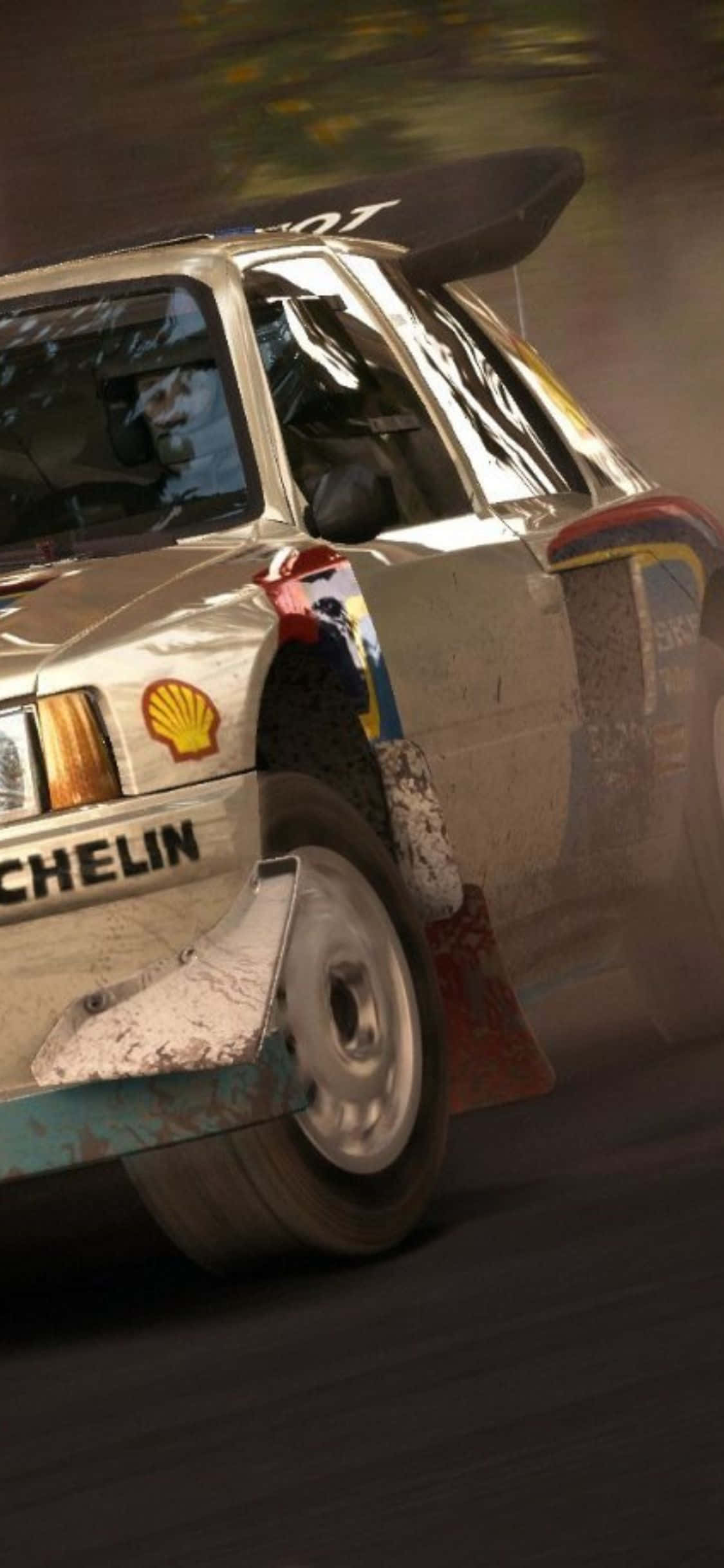 體驗《iPhone X Dirt Rally》的刺激賽道與激烈競賽 壁紙 — 一輛泥濘的拉力賽車在森林賽道上飛馳，揚起泥土和水花，車手專注地握著方向盤。