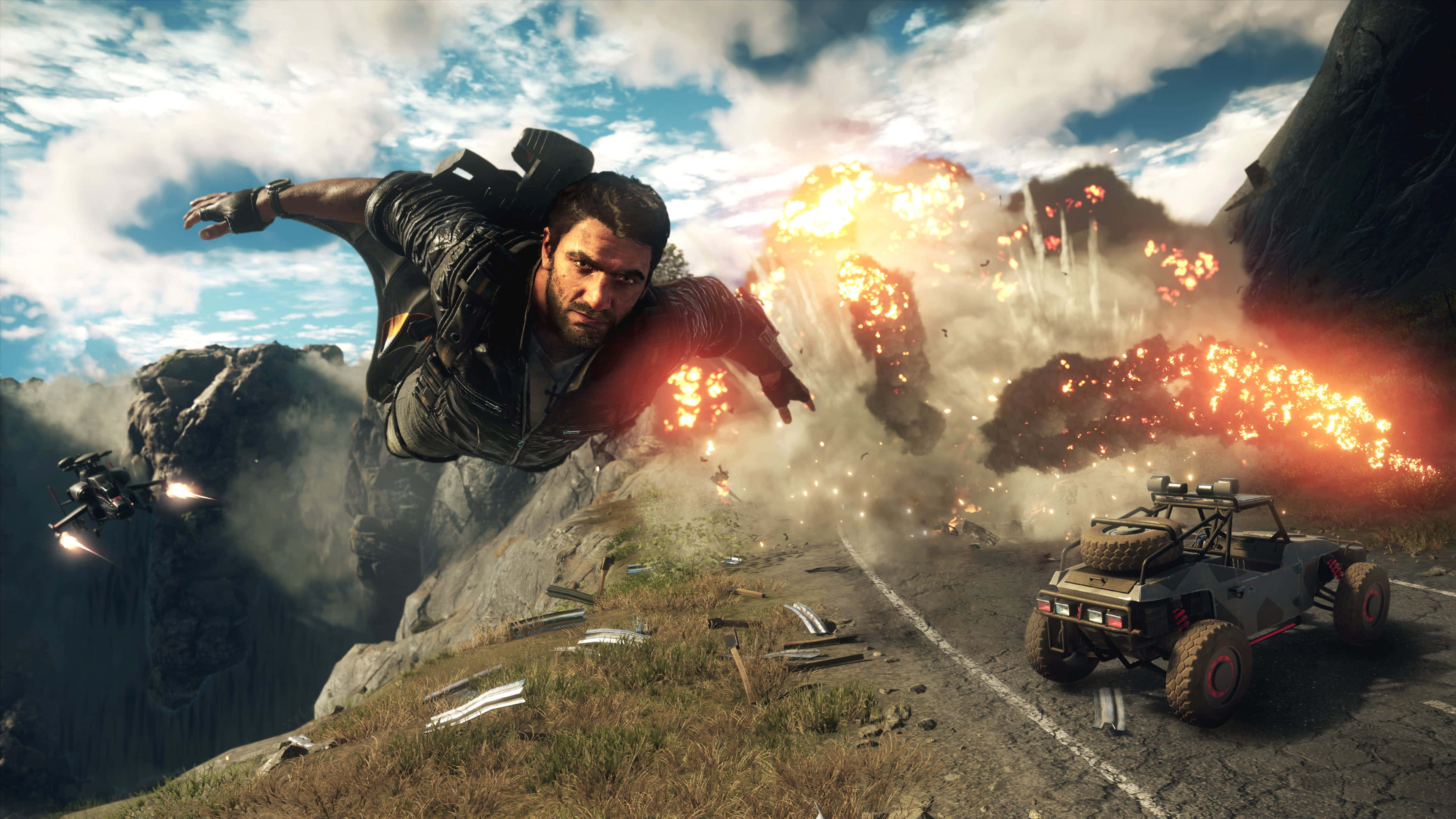 體驗《Just Cause 4》的腎上腺素狂潮！ 壁紙 — 一名男子在山路上空飛翔，身後爆炸四起，一輛堅固的車輛疾速前進。