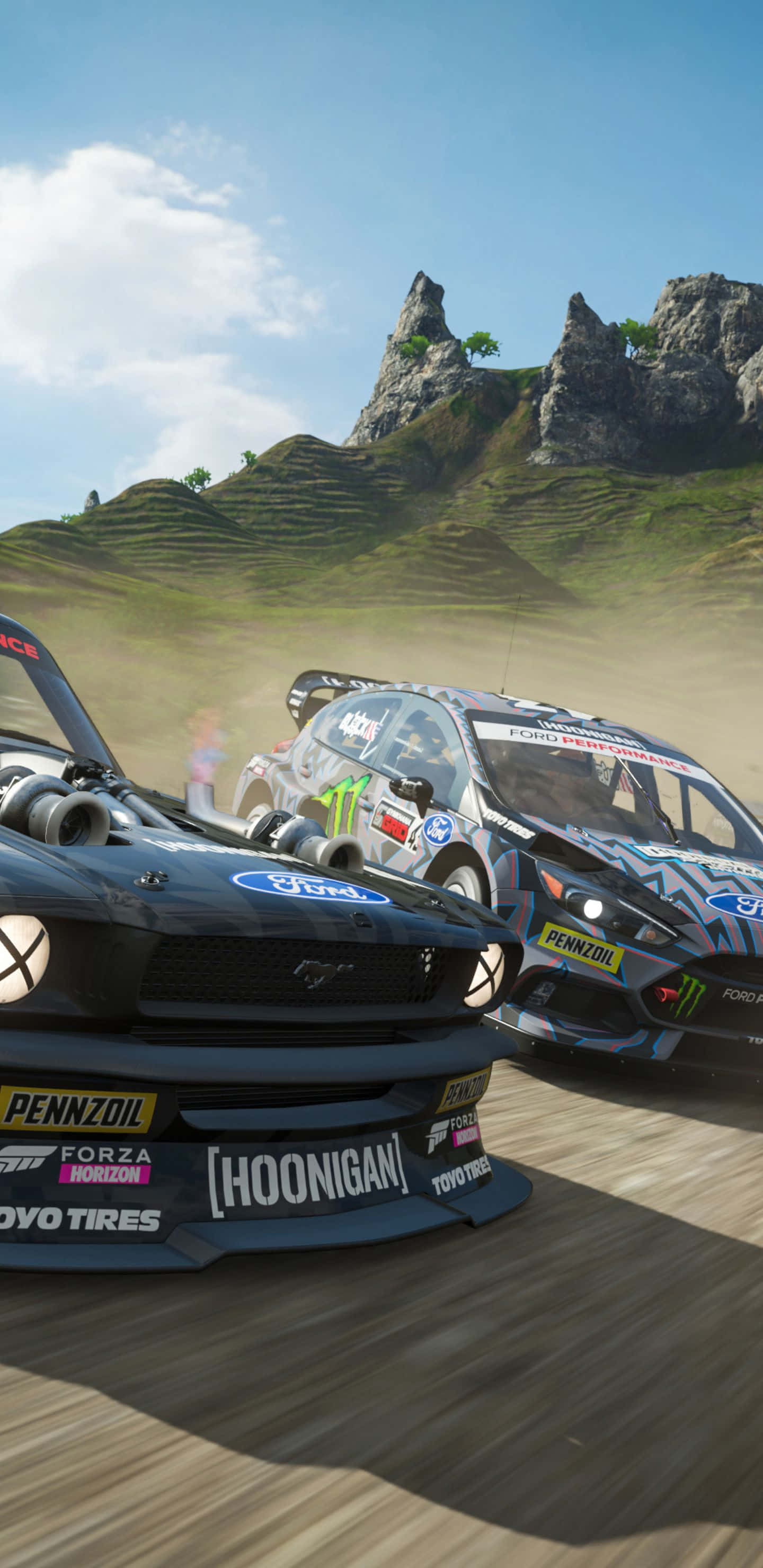 體驗 Pixel 3XL 的全速力量與 Forza Horizon 4 的震撼視覺 壁紙 — 兩輛拉力賽車在塵土飛揚的山路上激烈競速，周圍是岩石山峰和綠色山丘，天空湛藍明亮。