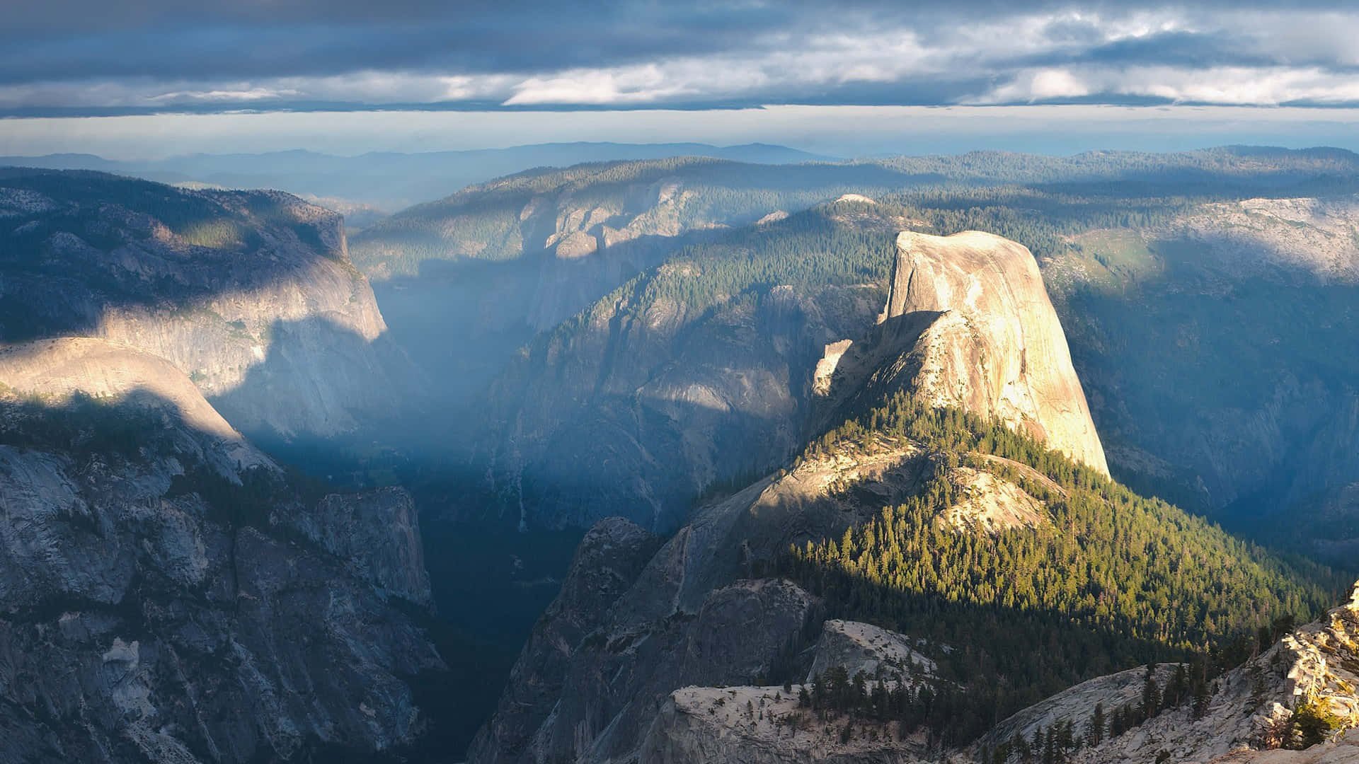Half Dome 山峰沐浴在陽光中，下方是森林覆蓋的山坡和霧氣瀰漫的山谷。