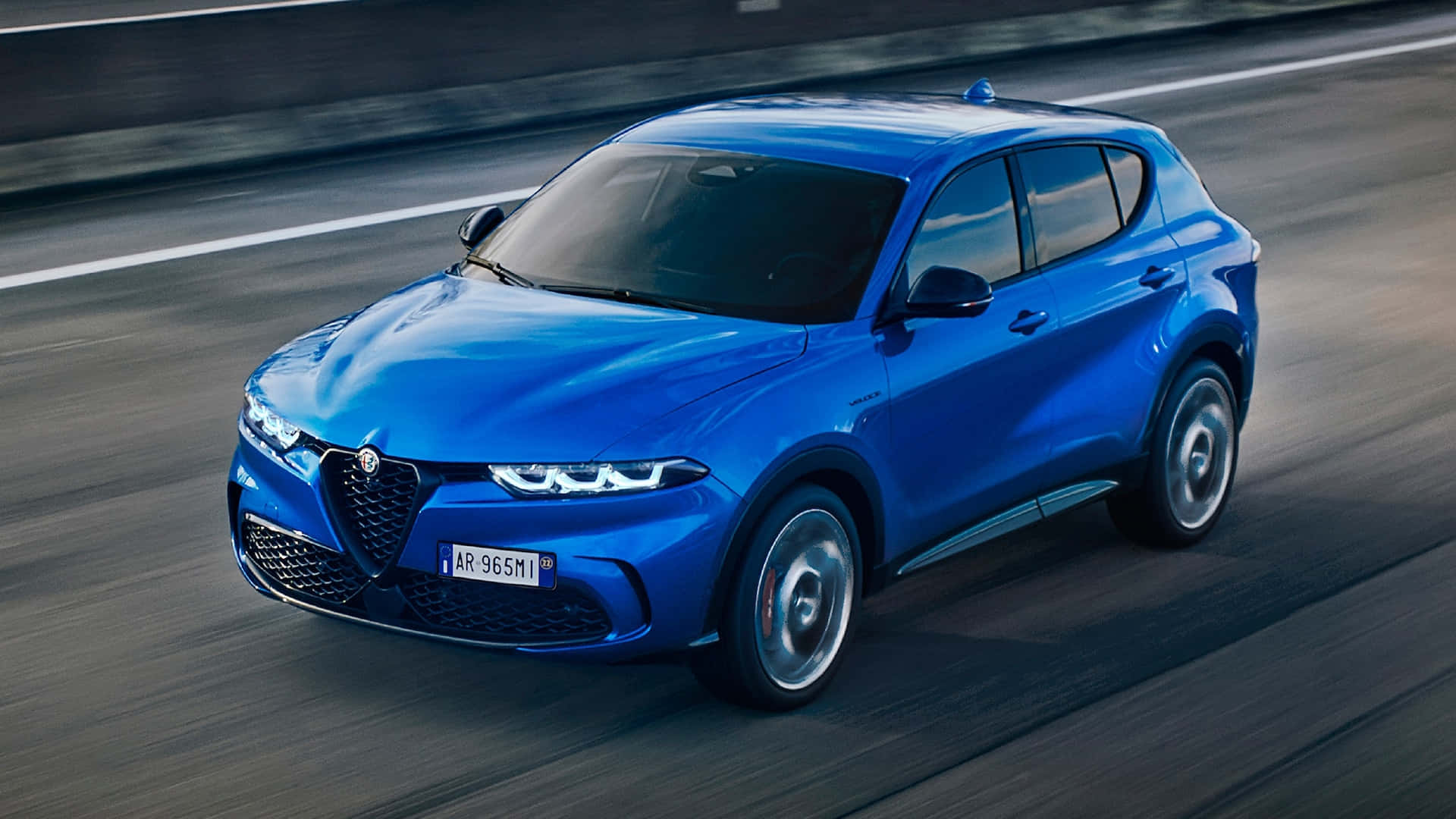 體驗Alfa Romeo的速度與優雅 壁紙 — 一輛充滿活力的藍色 Alfa Romeo SUV 在模糊的高速公路上疾馳，動態模糊強調了其動態運動。