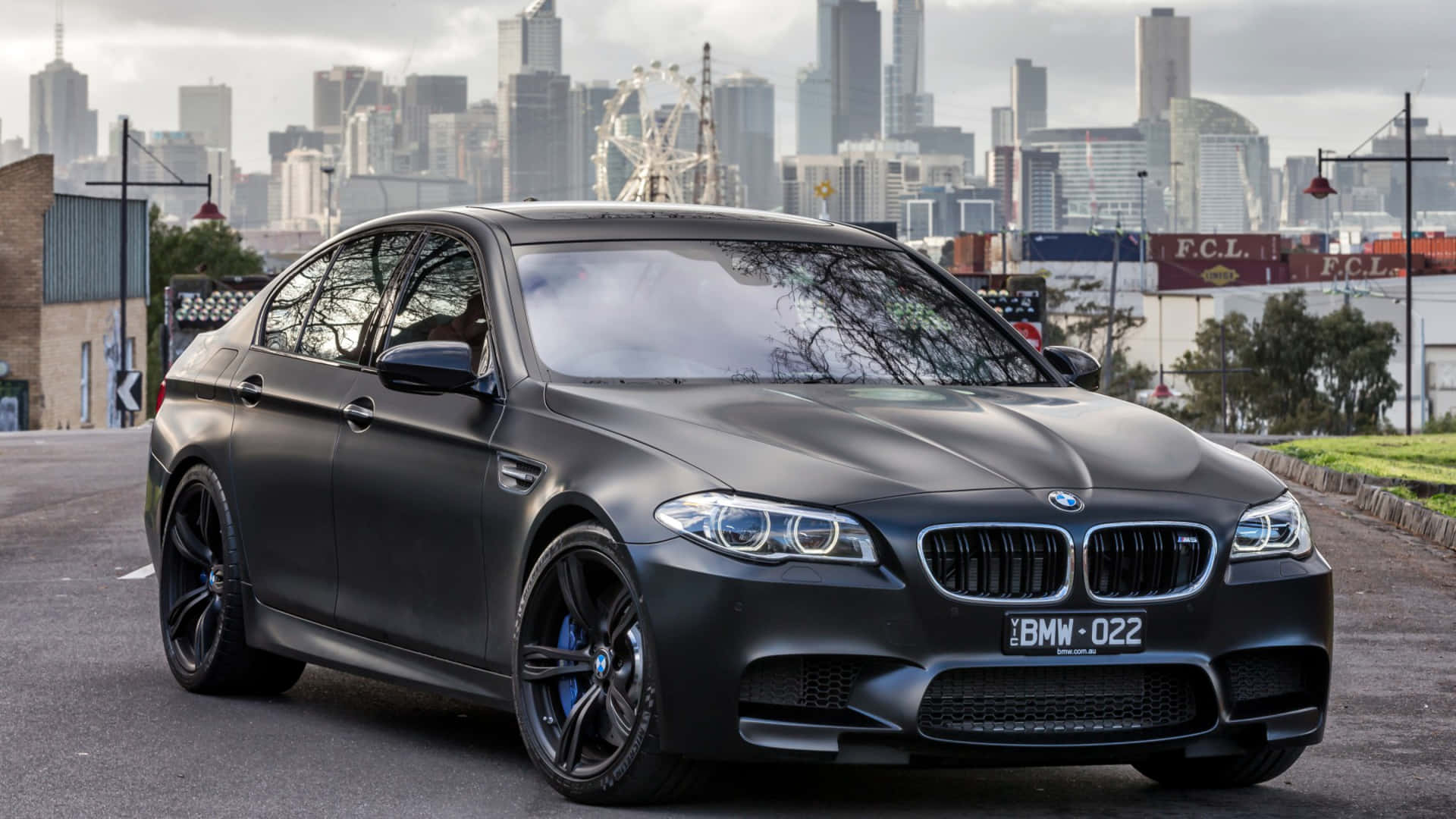 啞光黑色BMW M5停泊在摩天輪前的城巿天際線。
