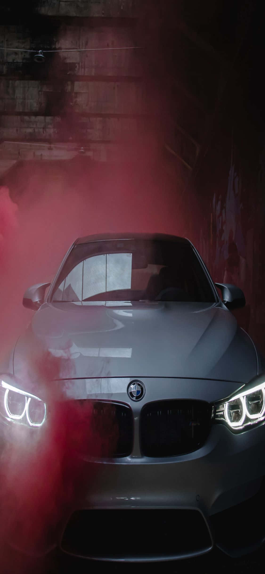 體驗BMW與iPhone X的極致奢華 壁紙 — 一架時尚的銀色BMW跑車在昏暗的混凝土隧道中，透過旋轉的紅色煙霧發出明亮的車頭燈光芒。
