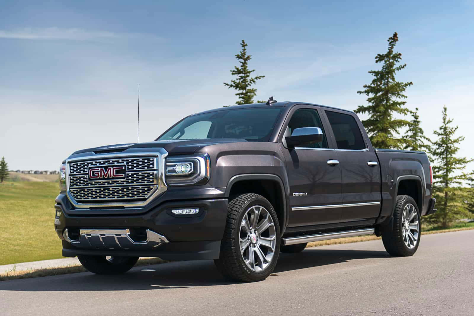 體驗GMC的豪華駕馭 壁紙 — 一架時尚的深灰色 GMC Sierra Denali 貨卡停在鋪砌的道路上，周圍有常綠樹和草地，天空清澈湛藍。