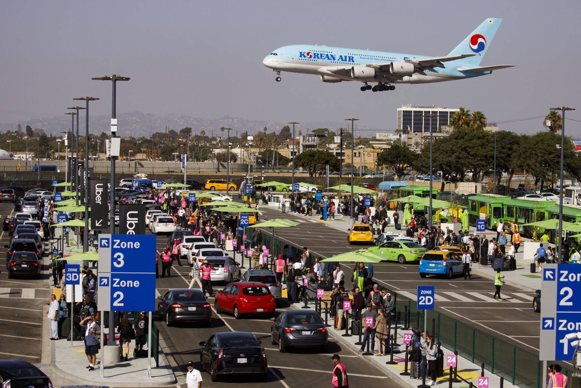 大韓航空飛機在擠滿乘客和綠色雨傘的繁忙機場的士區上空降落。
