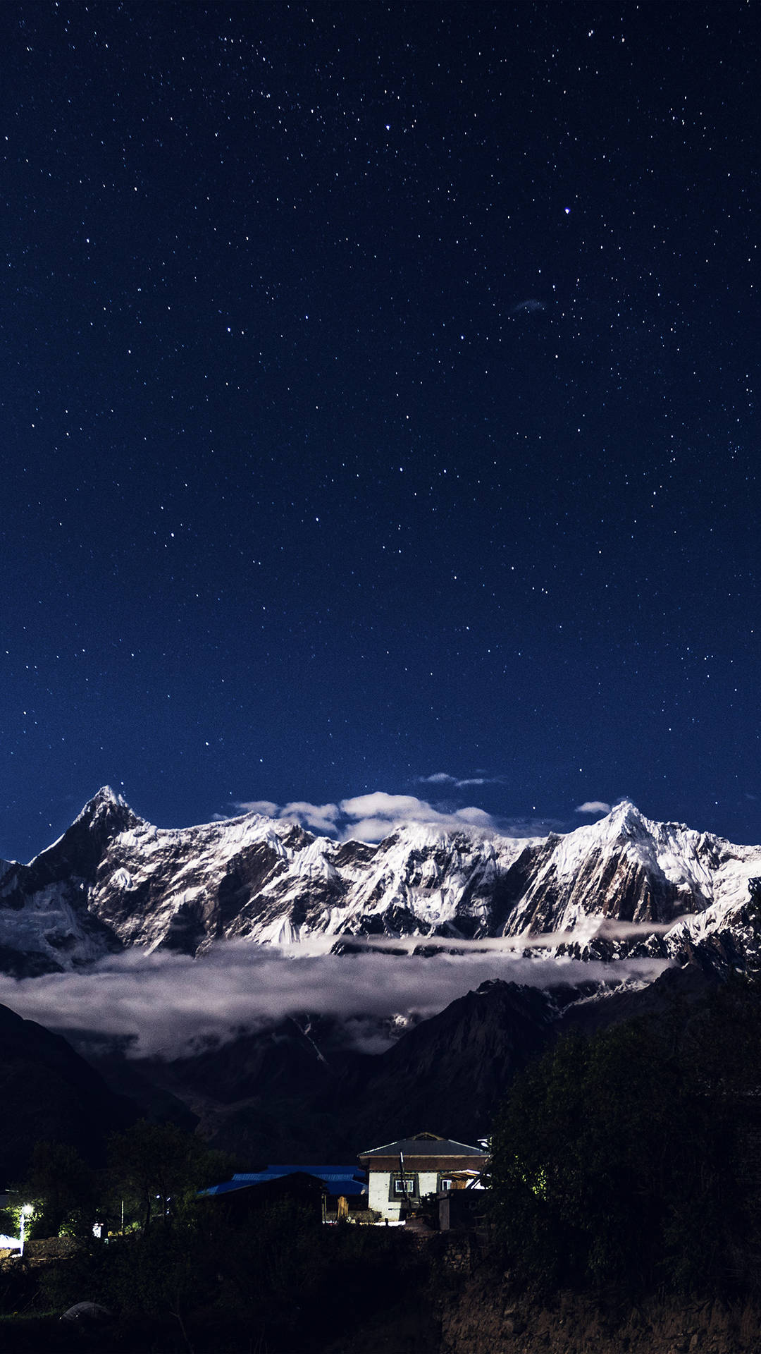 星空夜幕下的積雪山峰，山谷中亮燈的房子。