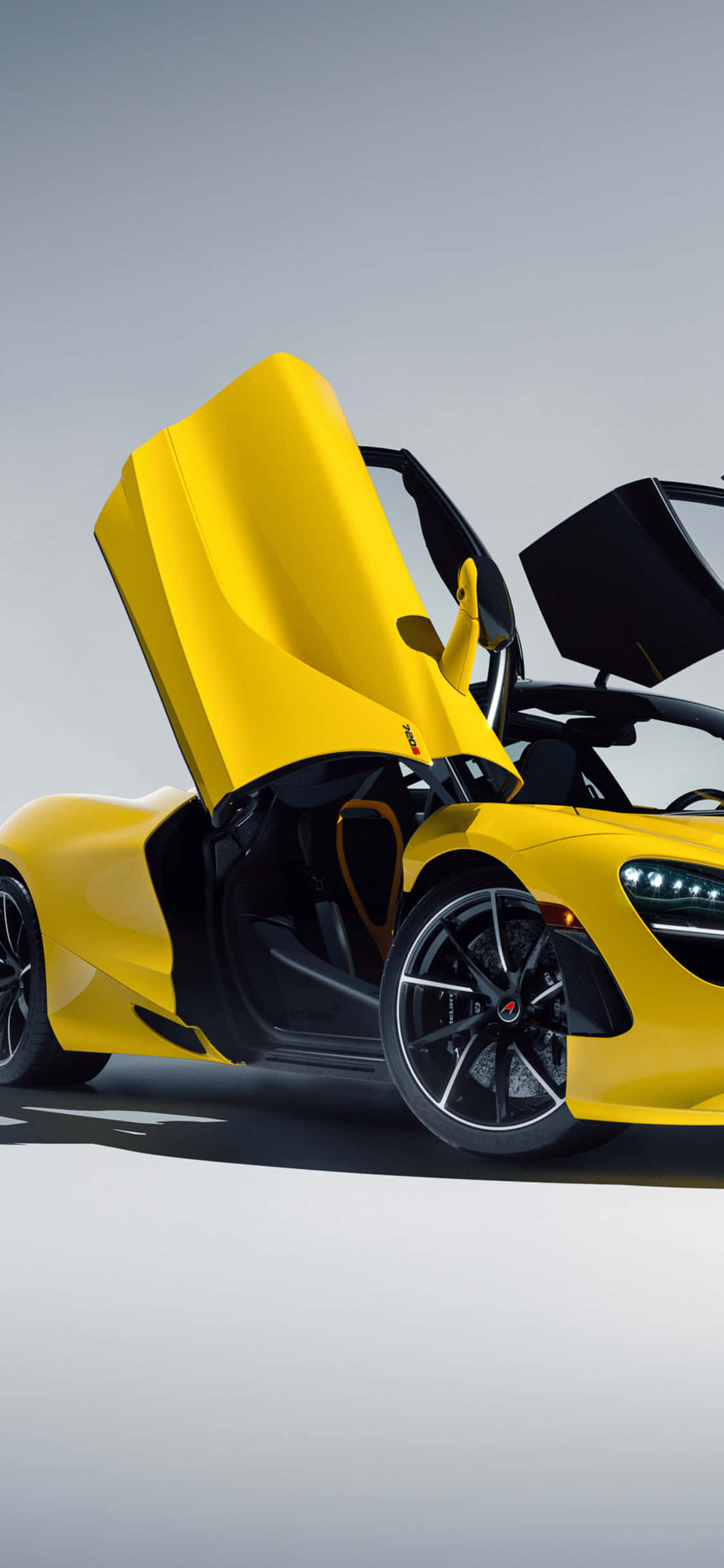 體驗奢華與高階性能的完美結合——iPhone XS McLaren 720S 壁紙 — 一輛鮮黃色的McLaren跑車，鷗翼門打開，背景是簡約的灰色工作室。