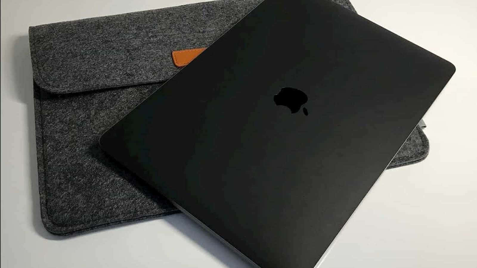 黑色MacBook放在灰色氈套上，帶橙色細節，置於白色表面
