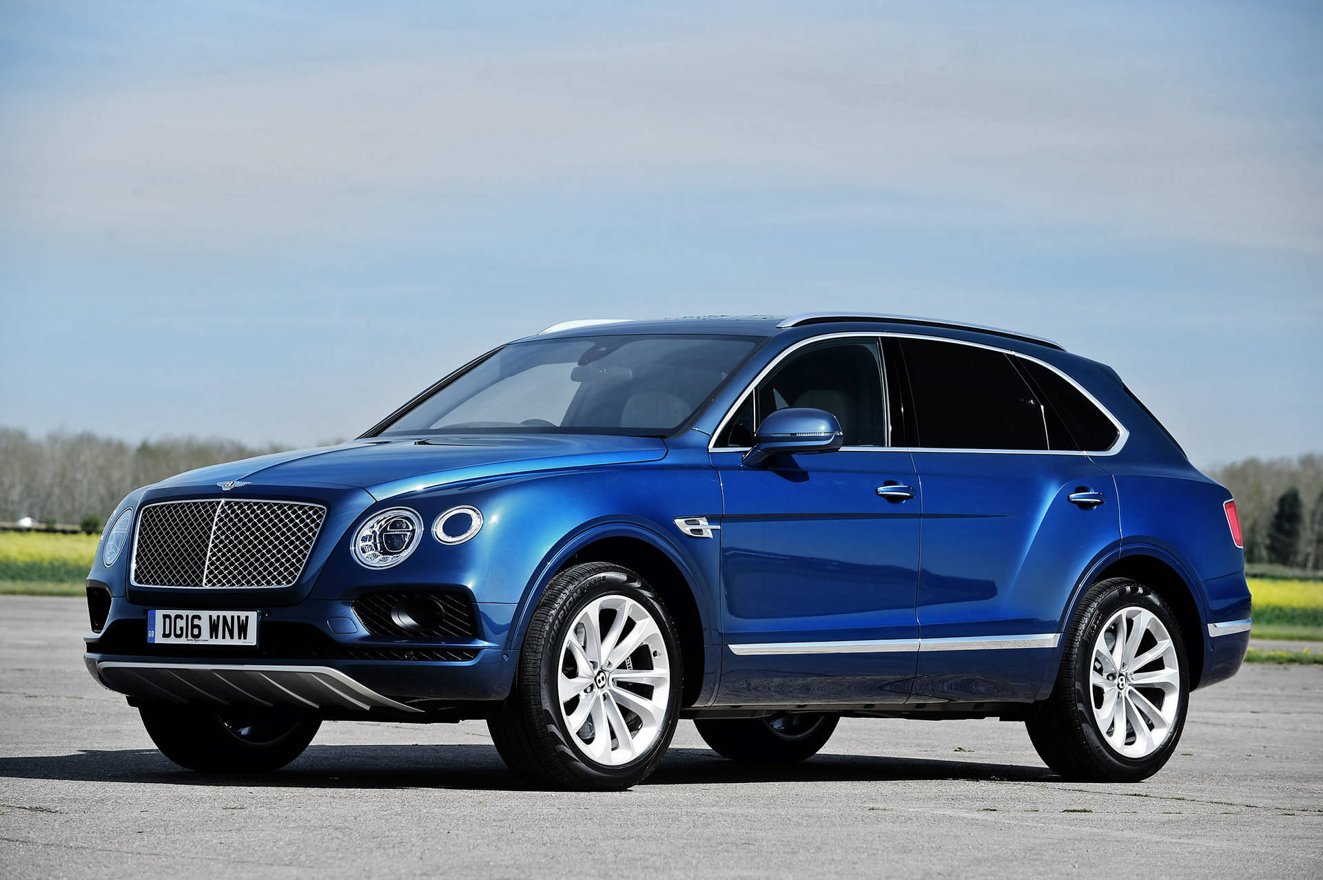 藍色賓利Bentayga SUV停在鋪砌路面上，後面有樹木和天空。
