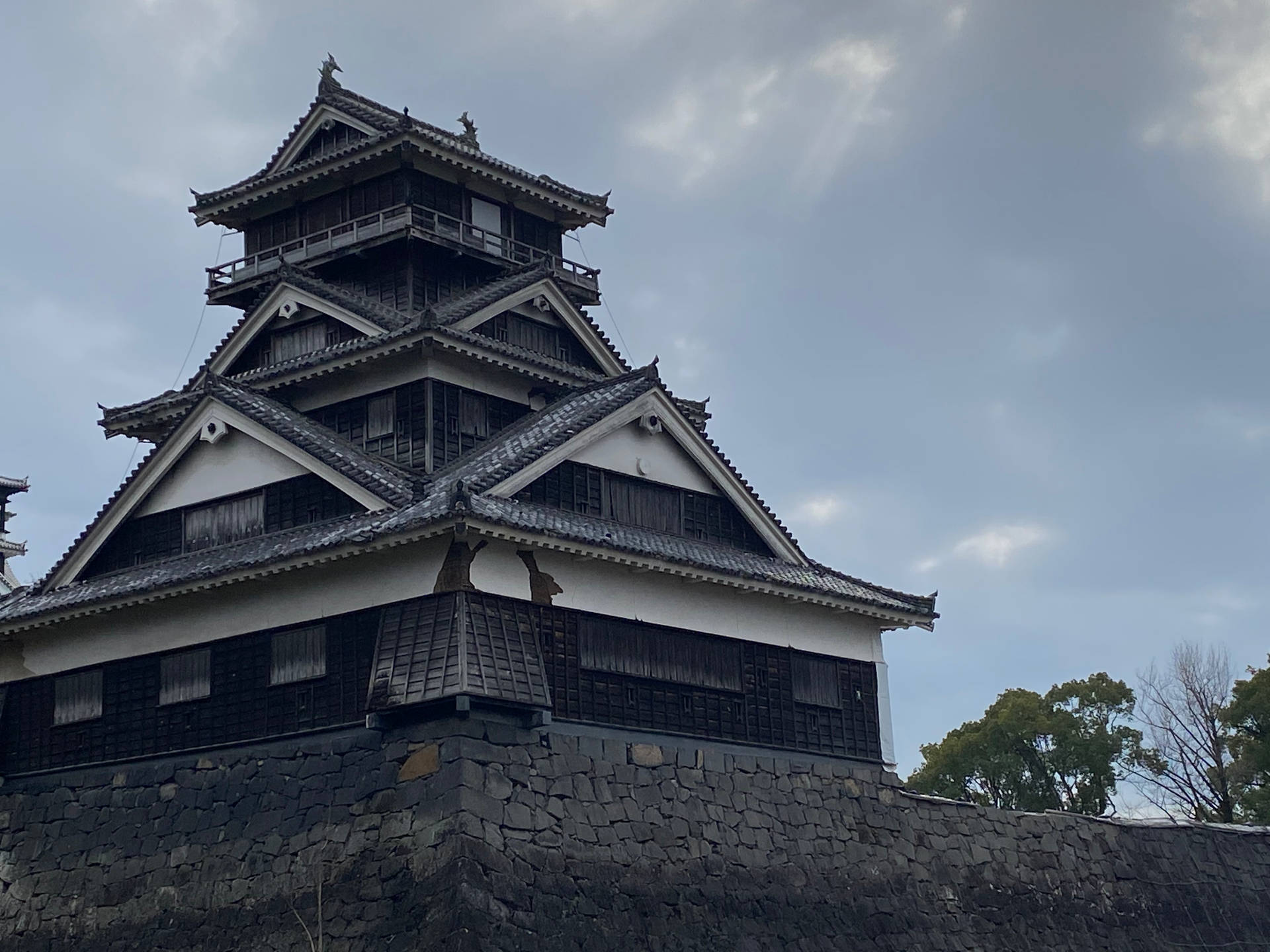 傳統日本城堡塔樓，層疊屋頂和石質底座，在多雲的天空下。