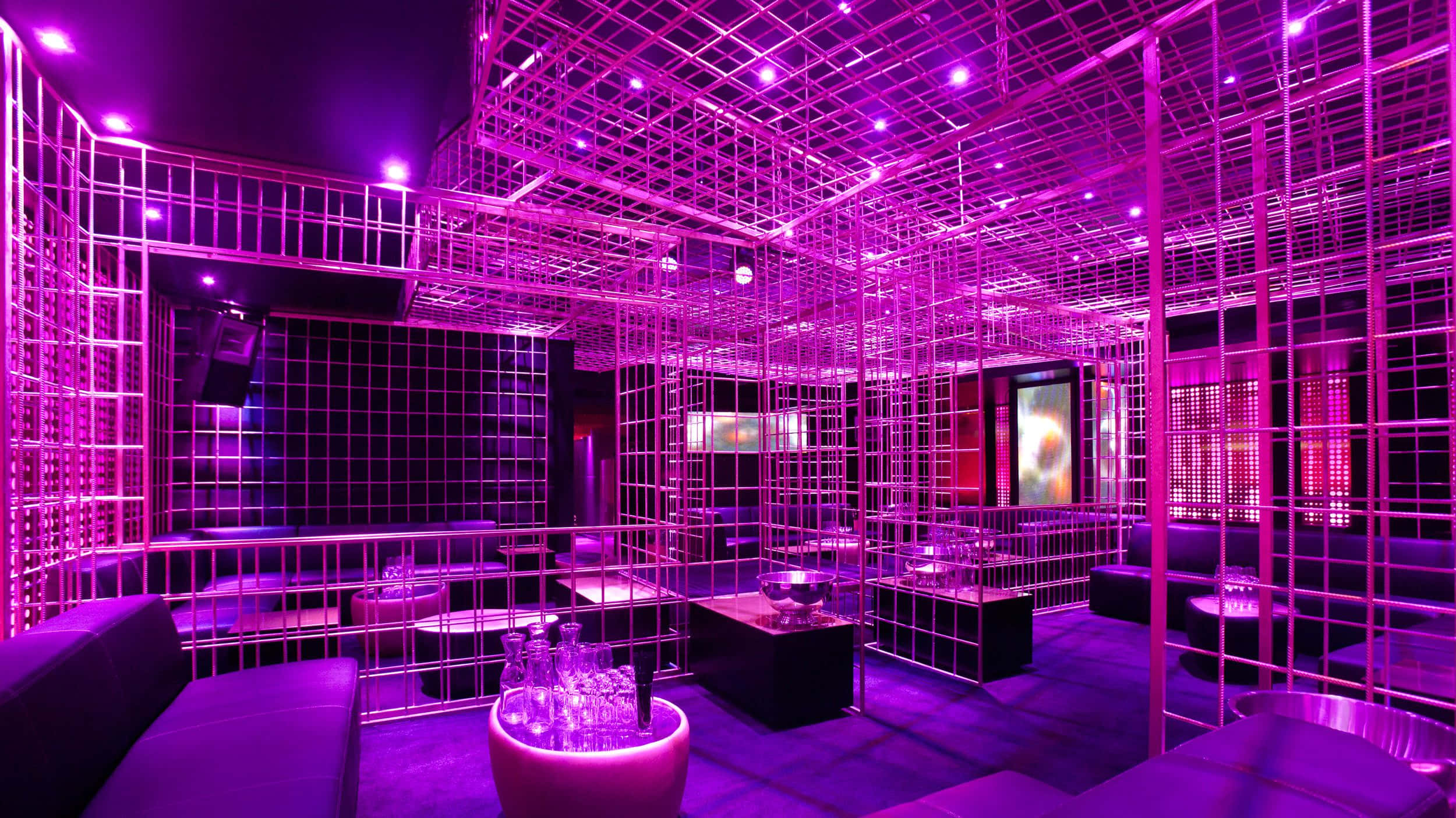 體驗最完美的夜店體驗！ 壁紙 — 一間充滿未來感的夜店，沐浴在電光紫色燈光中，帶有發光的網格結構和時尚的黑色家具。
