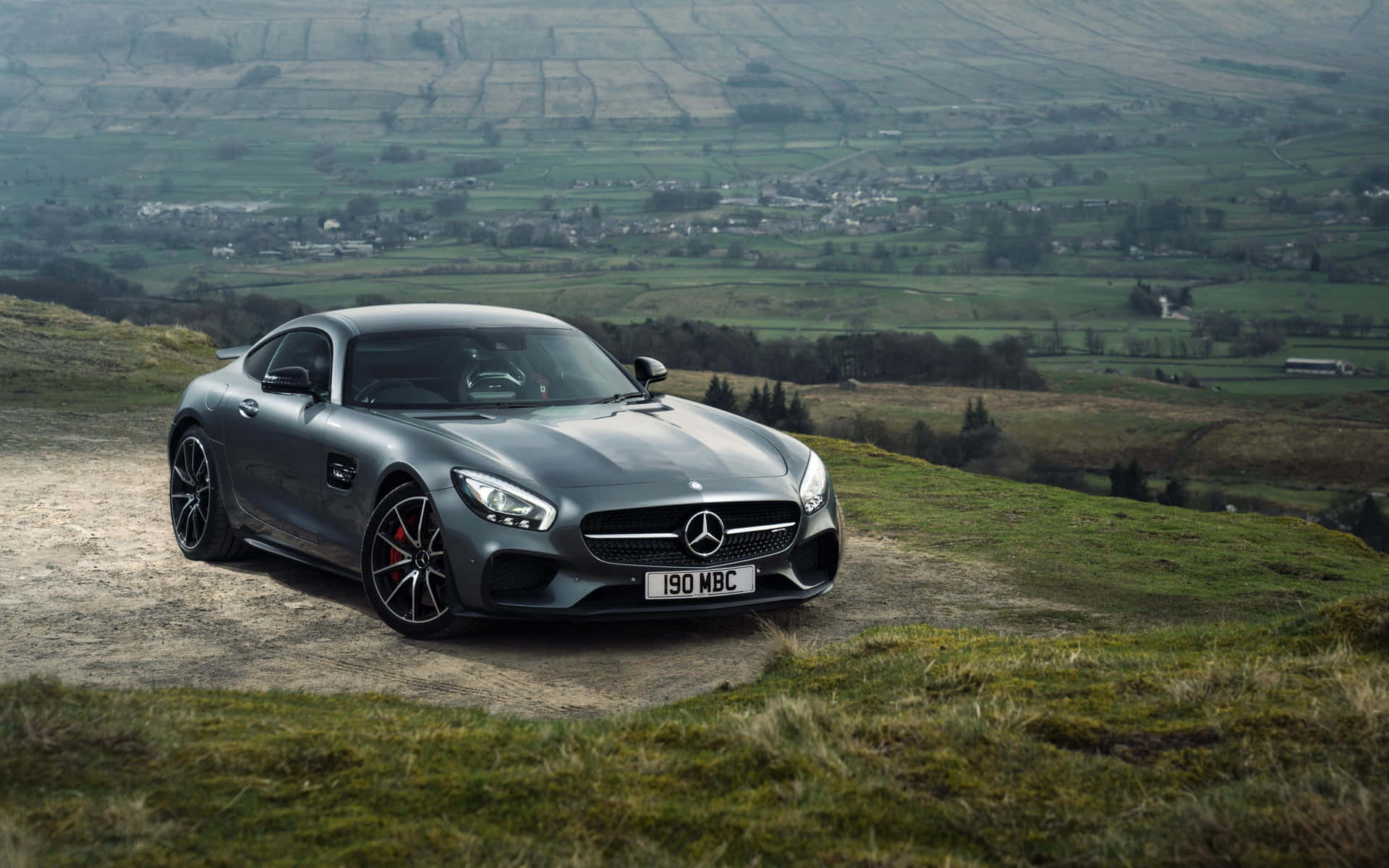 日落時分，灰色 Mercedes-AMG GT 停在青草山坡上，俯瞰鄉村山谷。