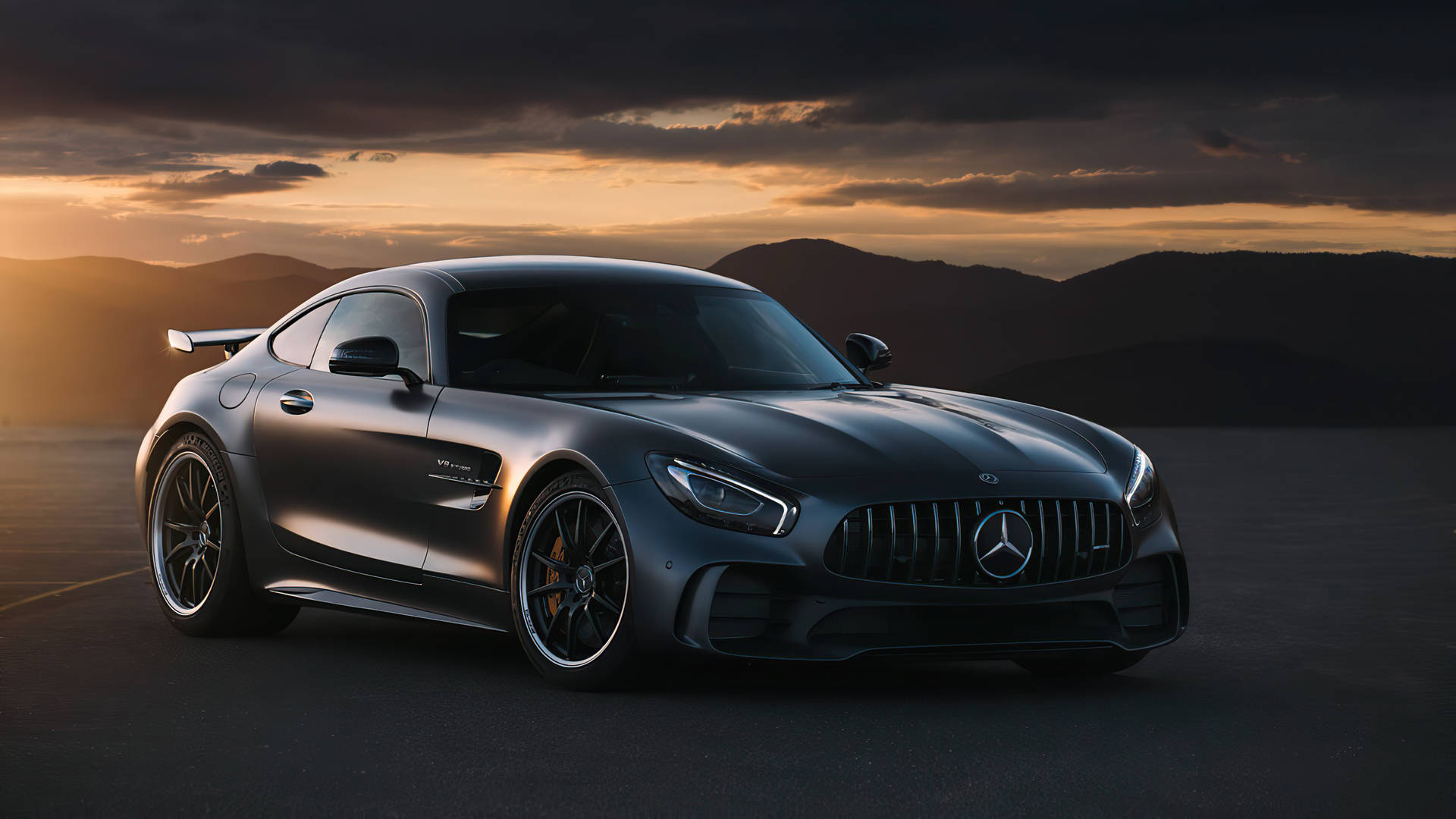 啞光灰色Mercedes-AMG GT跑車在日落時分停泊在開闊道路上，背景有山脈。
