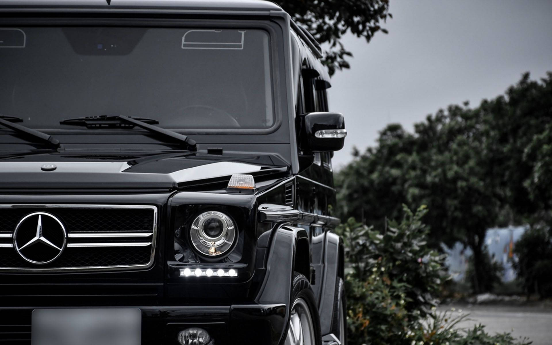 黑色 Mercedes-Benz G-Class SUV 停放在樹木附近，天空多雲。
