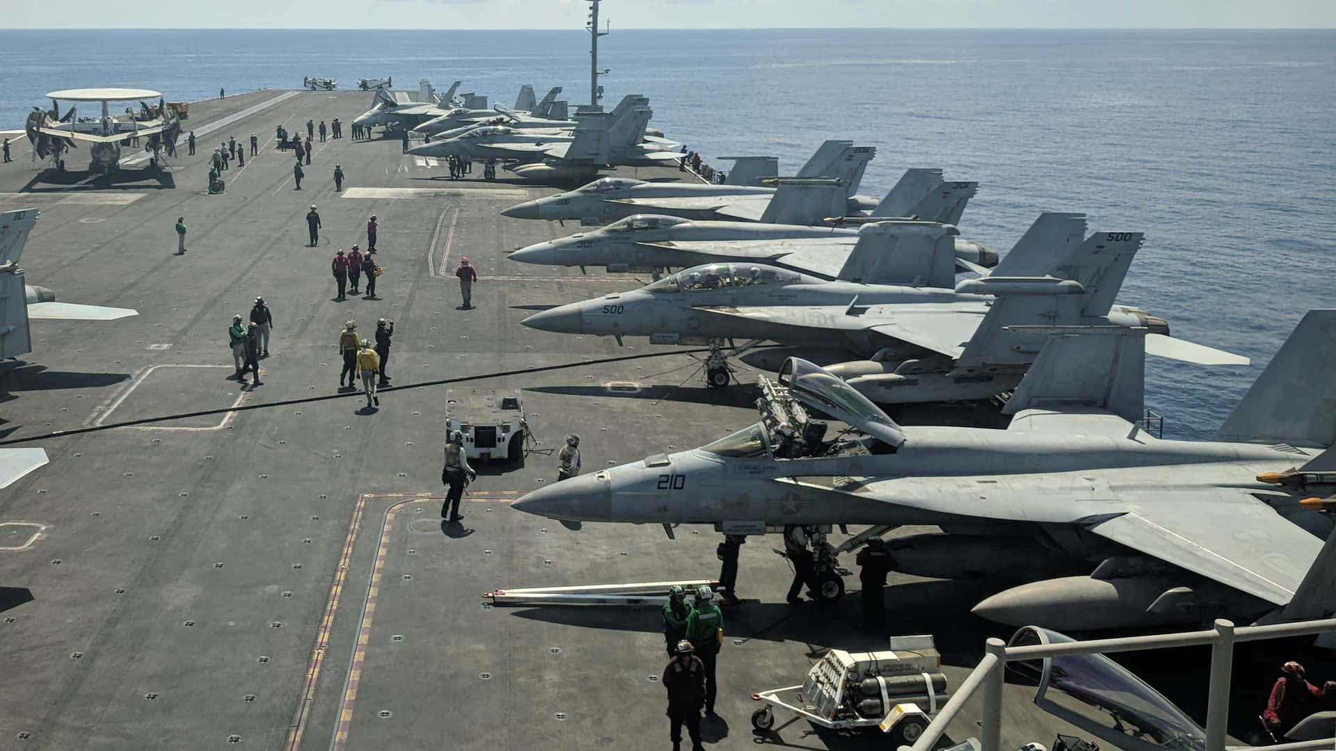 體驗海軍服役的刺激 壁紙 — 航空母艦甲板上，戰鬥機整齊排列，船員在明亮的日光下走動。