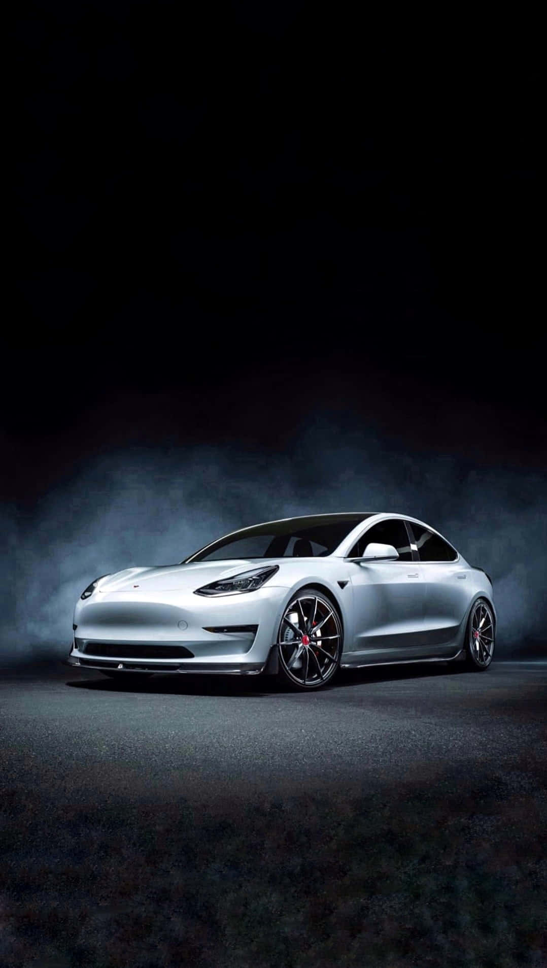 銀色Tesla Model 3在深色煙霧背景上被聚光燈照亮。