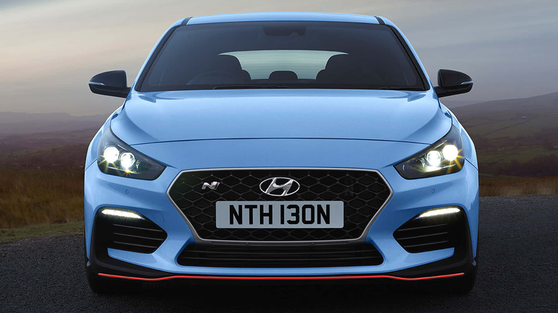 藍色Hyundai i30N跑車在山路上亮著車頭燈。