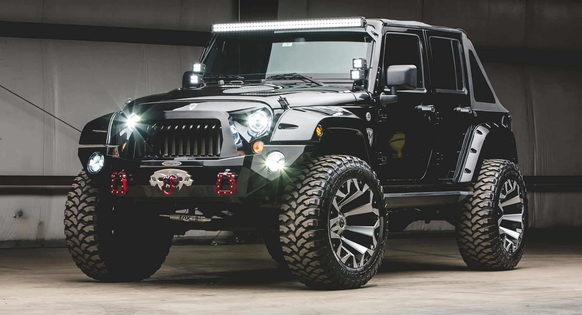 體驗經典Jeep Wrangler的越野之旅 壁紙 — 一輛黑色升高嘅Jeep Wrangler，配備超大輪胎同明亮LED燈，喺昏暗嘅車庫中顯眼地停泊。
