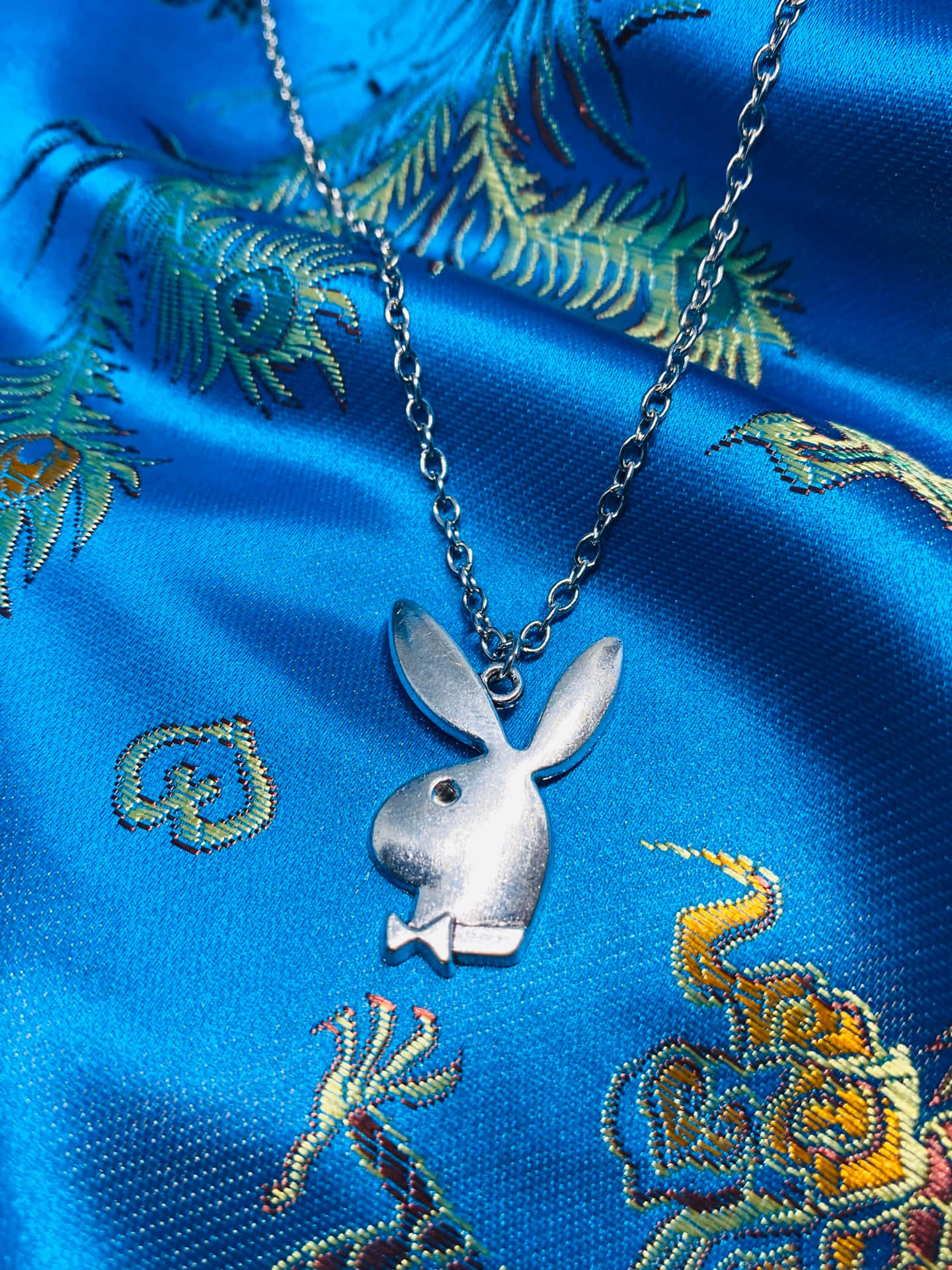 銀色Playboy兔仔吊墜項鍊在藍色刺繡緞布上。
