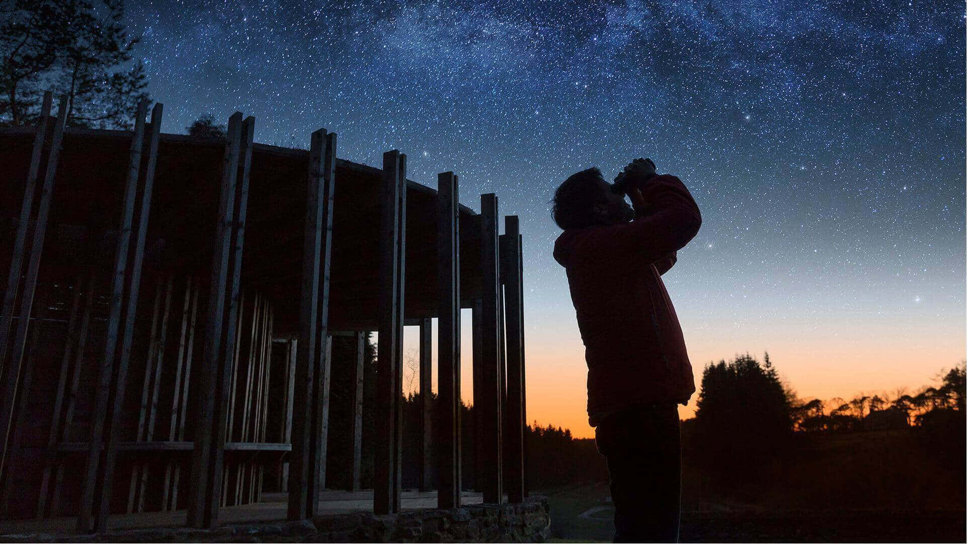 在木結構附近黃昏時使用雙筒望遠鏡觀星的人。