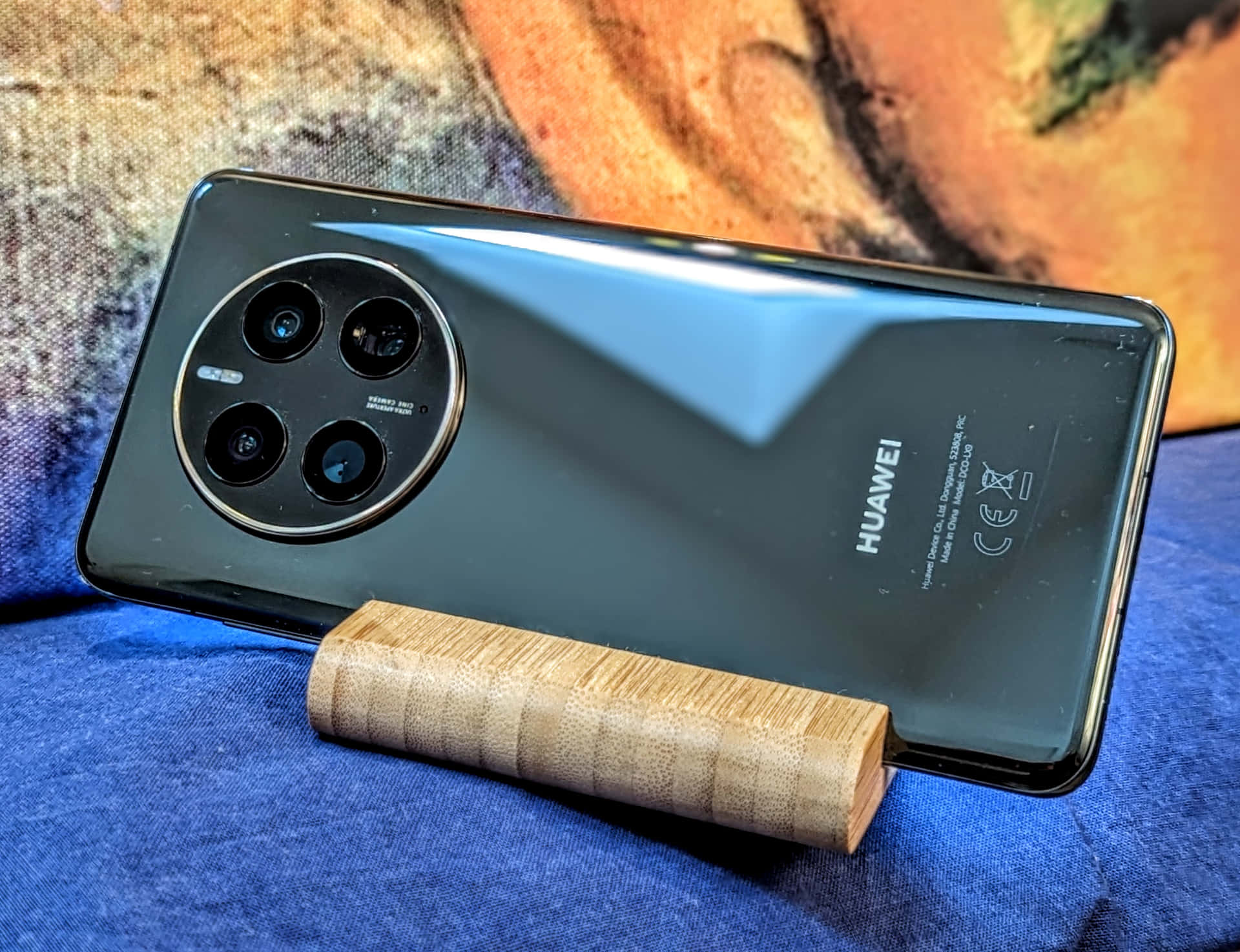 黑色Huawei手機，圓形鏡頭模組，木製支架，藍色布料背景。