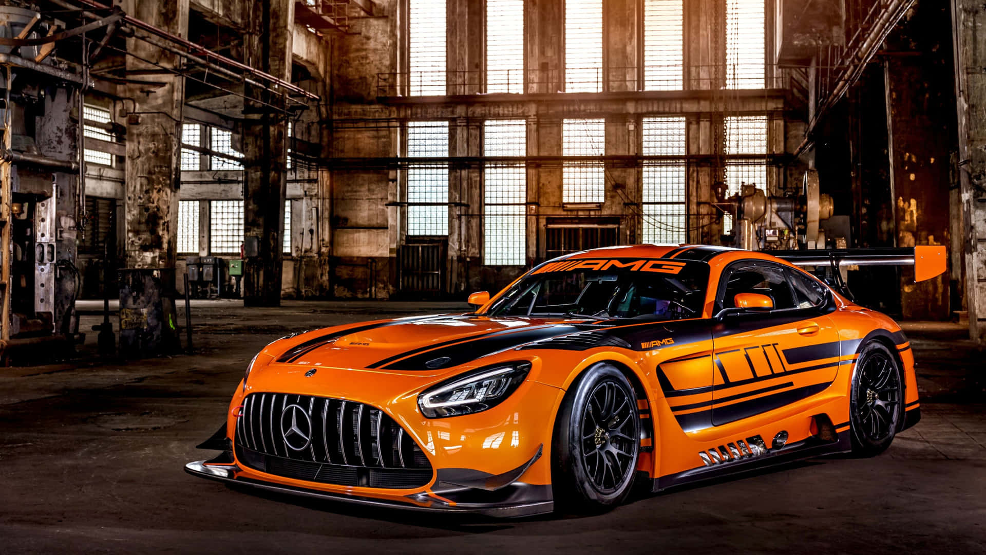 橙色 Mercedes-AMG GT3 賽車在生鏽的工業倉庫中，陽光透過窗戶照射進來。