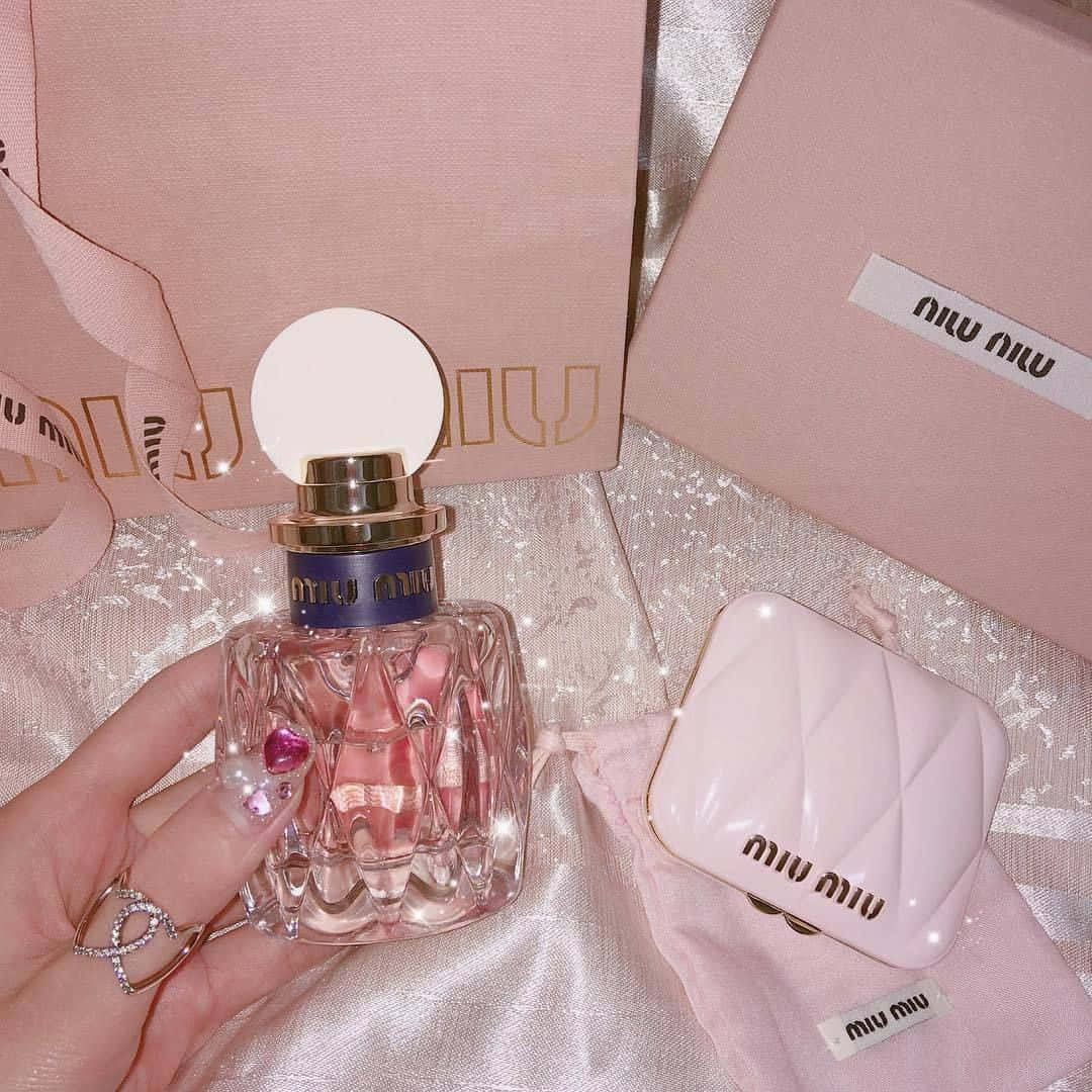手拿著Miu Miu香水瓶，配上相配的粉紅色配件，放在閃閃發光的布料上。