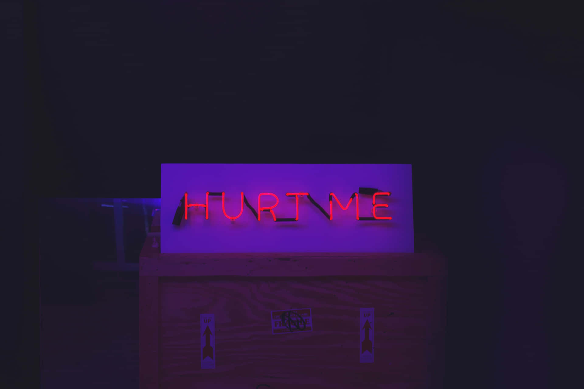 黑暗中木箱上寫著 hurt me 的紅色霓虹燈牌