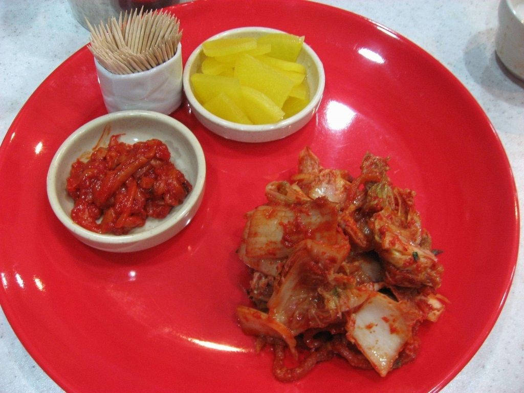 紅色碟子，上面有泡菜、醃蘿蔔和牙籤，供食用。