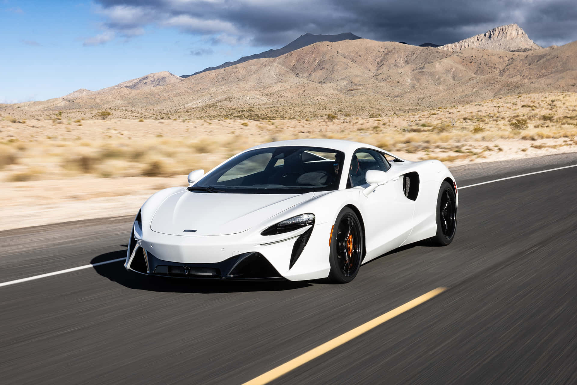 白色McLaren跑車在沙漠高速公路上飛馳，背景有山脈。