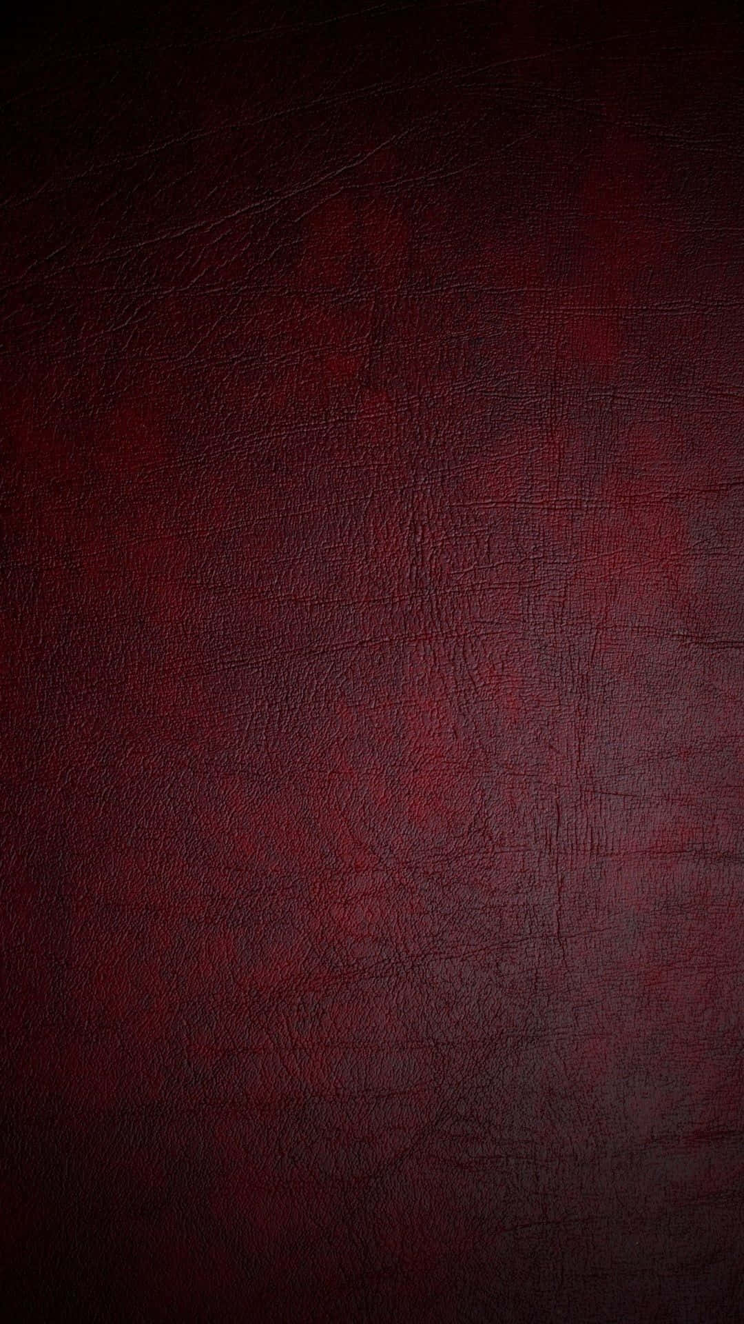 體驗黑紅 iPhone 的強大性能 壁紙 — 深紅色紋理皮革的微距特寫，帶有細微刮痕和天然粒面圖案。