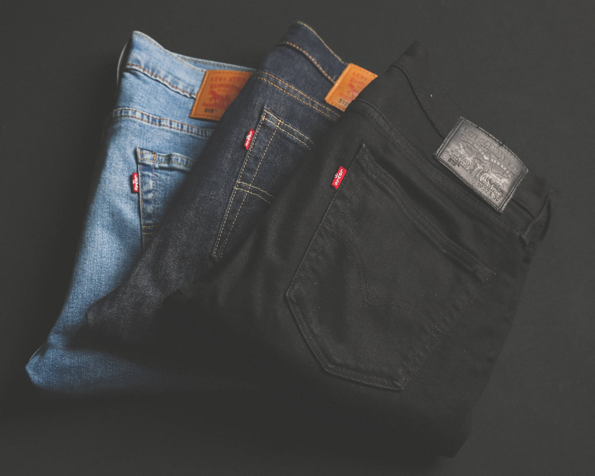 三條摺疊的Levi's牛仔褲，不同洗水，放在深色表面上。