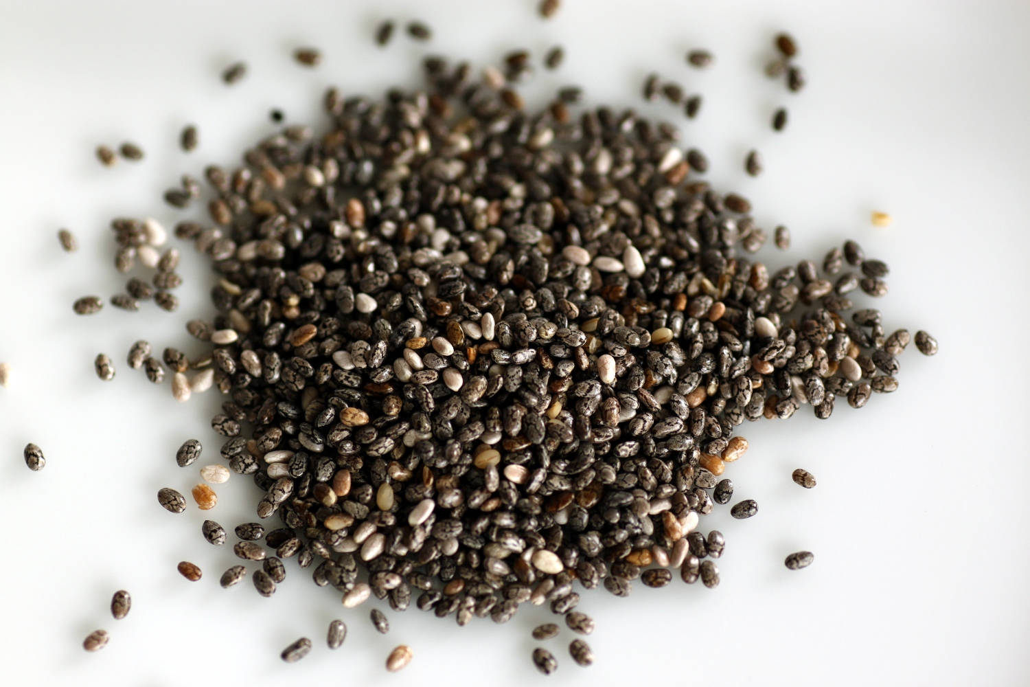 高品質營養奇亞籽圖像 壁紙 — 一堆深色和淺色奇亞籽的特寫，散落在明亮的白色表面上。