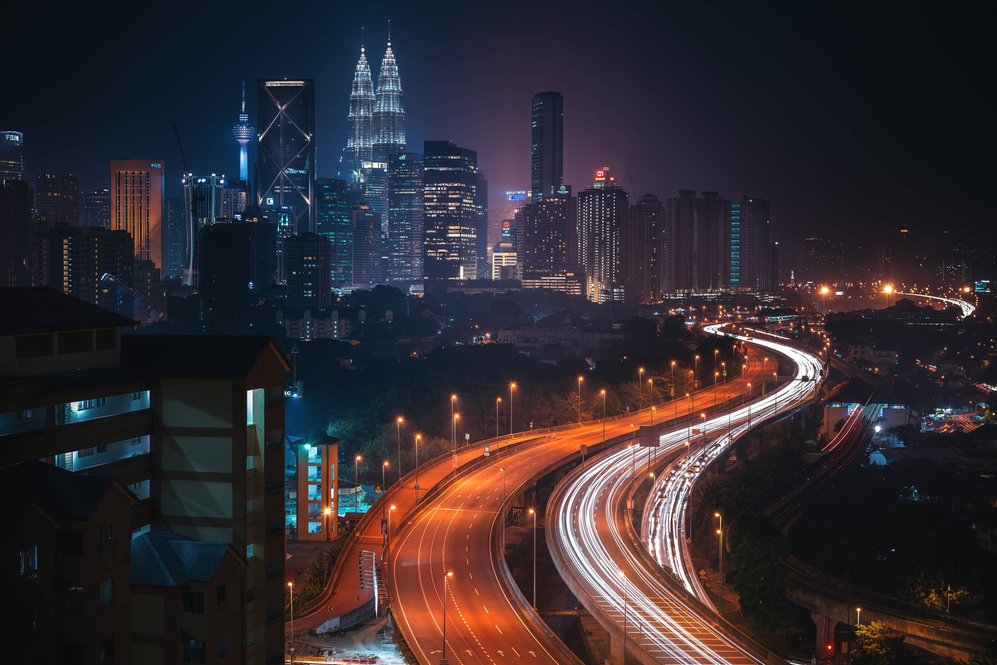高品質馬來西亞城市 壁紙 — 充滿活力的夜景城市景觀，閃爍的摩天大樓和蜿蜒高速公路上的車流光軌。