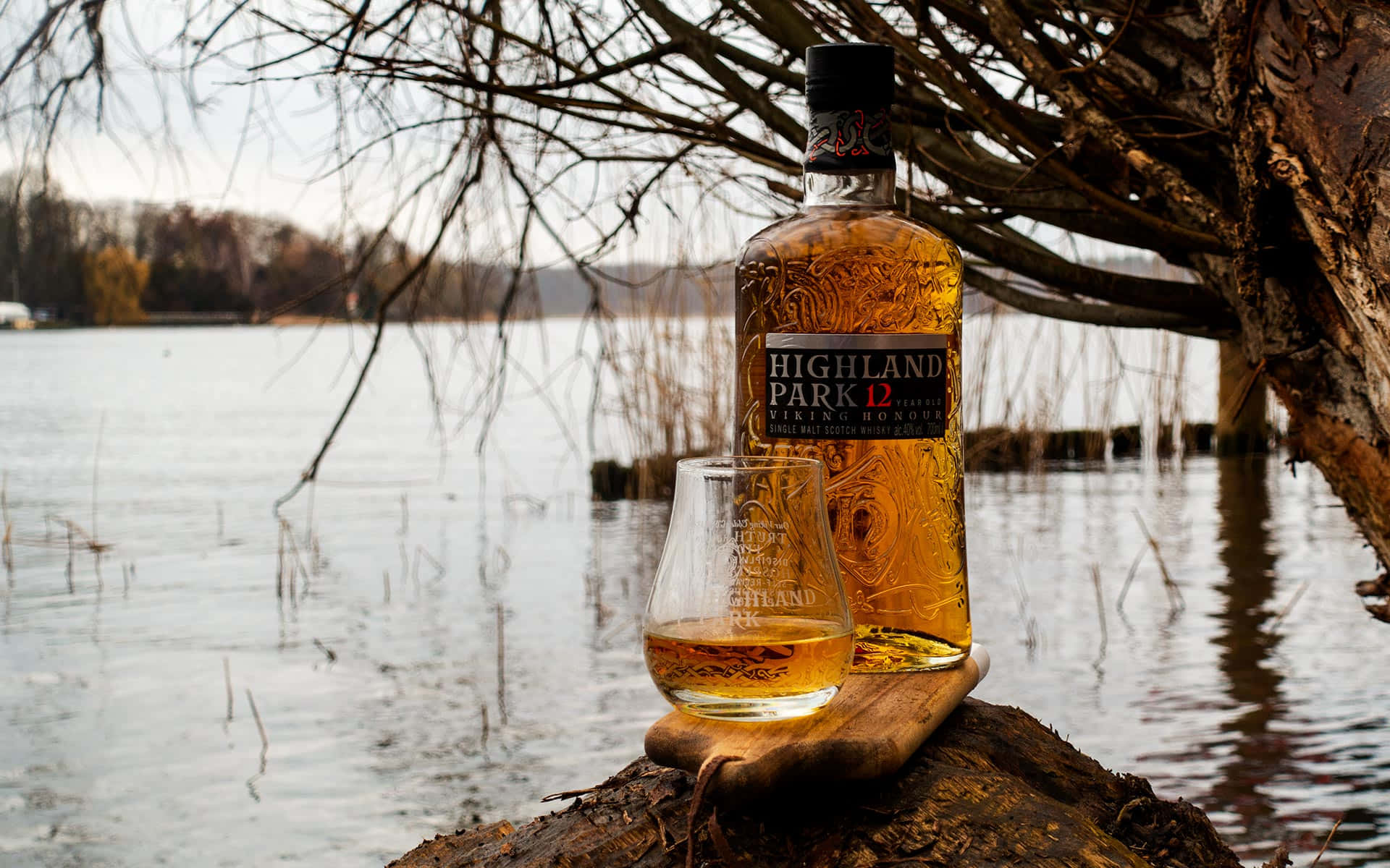 冬季湖邊木頭上的 Highland Park 威士忌瓶和酒杯。