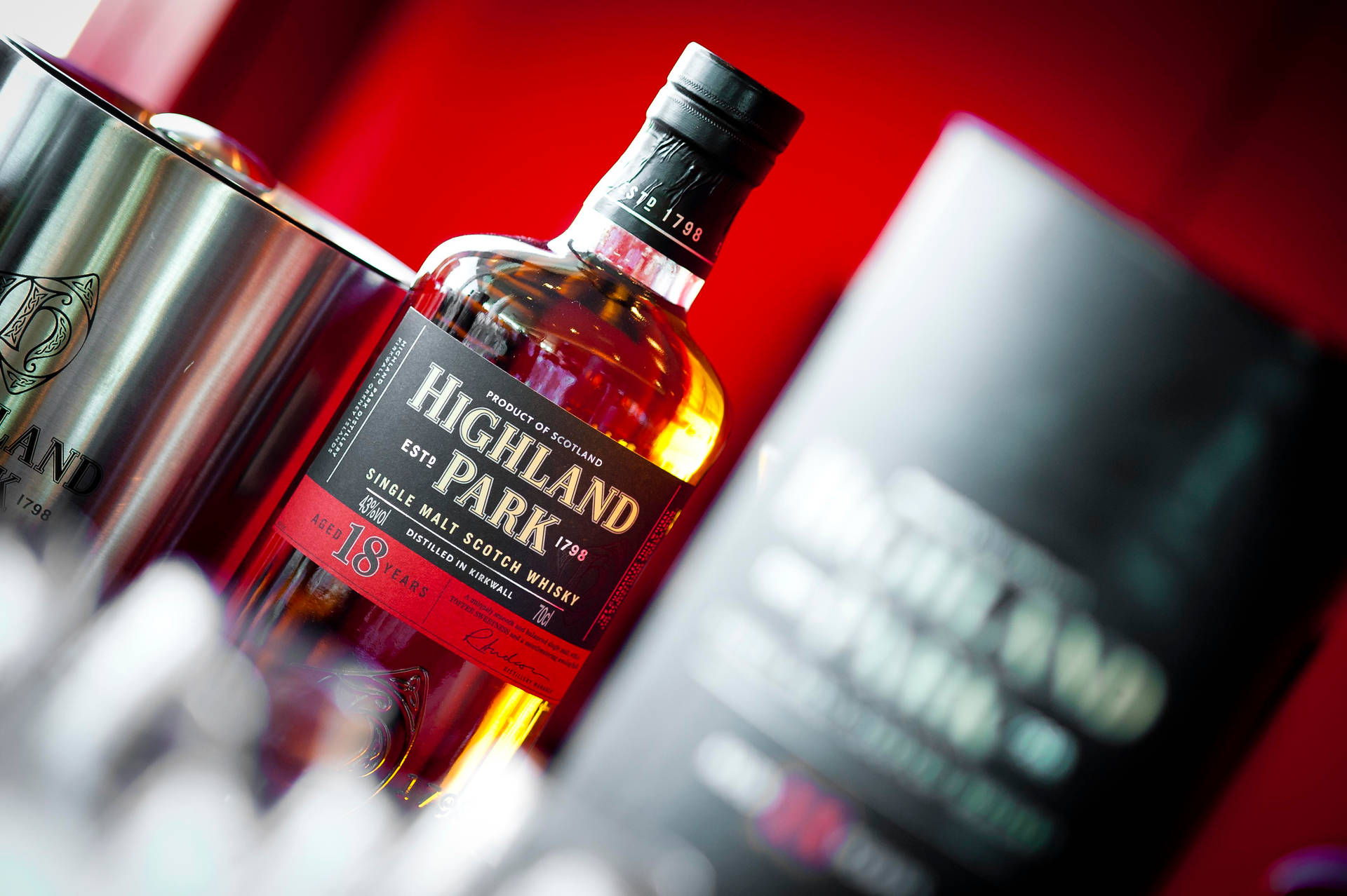 一瓶 Highland Park 18 年威士忌，附冰桶和盒子，置於紅色背景上。