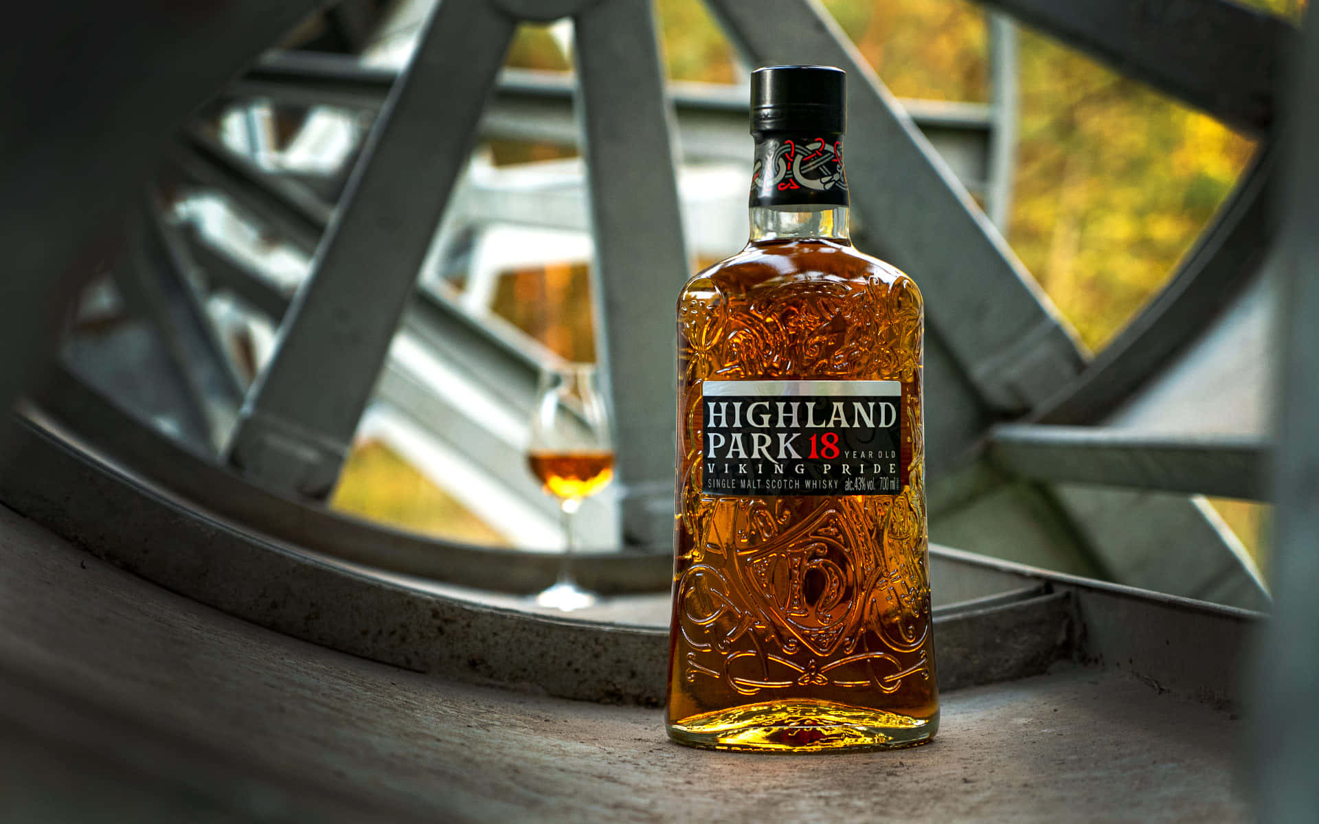 一瓶 Highland Park 威士忌旁邊放著一個玻璃杯，由金屬條和秋葉框住。
