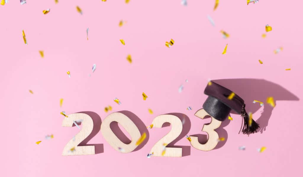畢業帽和木製2023字母，粉紅色背景上紙屑飄落。