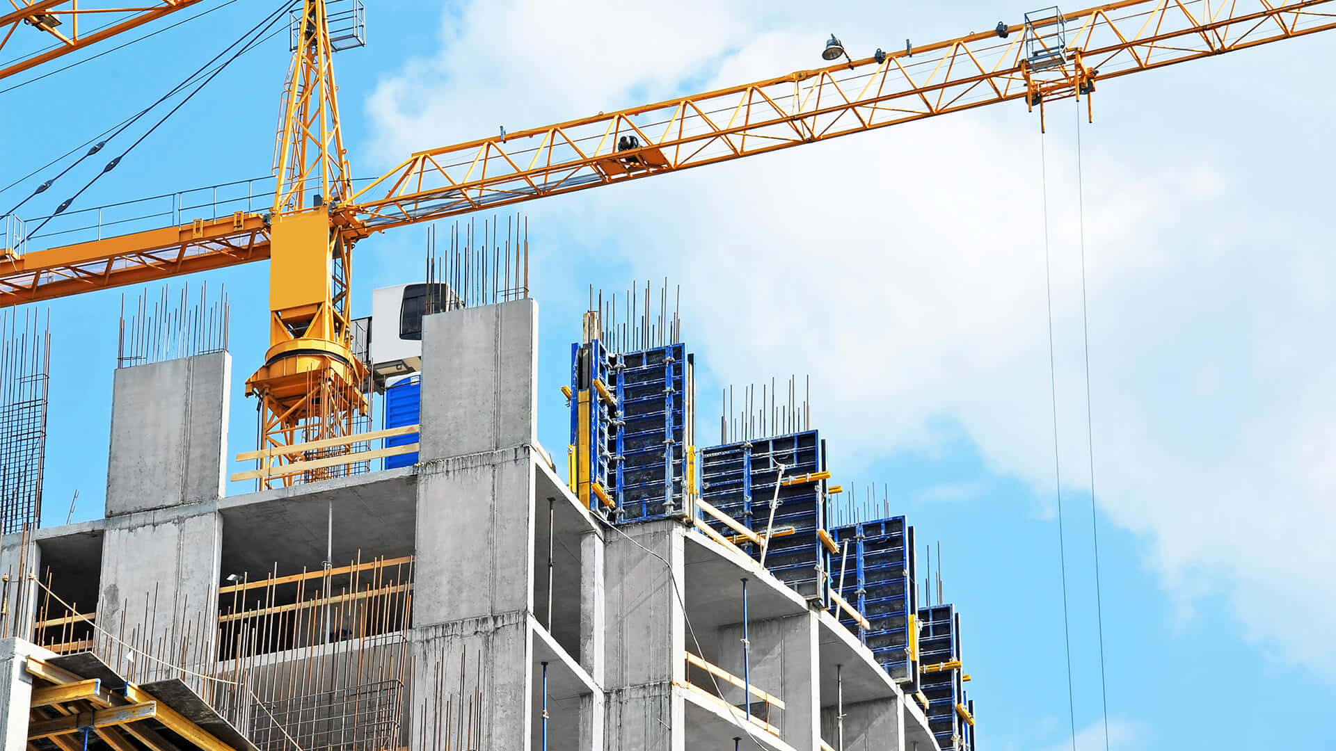 高層混凝土建築與起重機場景 壁紙 — 一座高聳的黃色起重機在明亮的藍天下，主導著一棟正在施工的多層混凝土建築，建築物有外露的鋼筋和藍色模板。