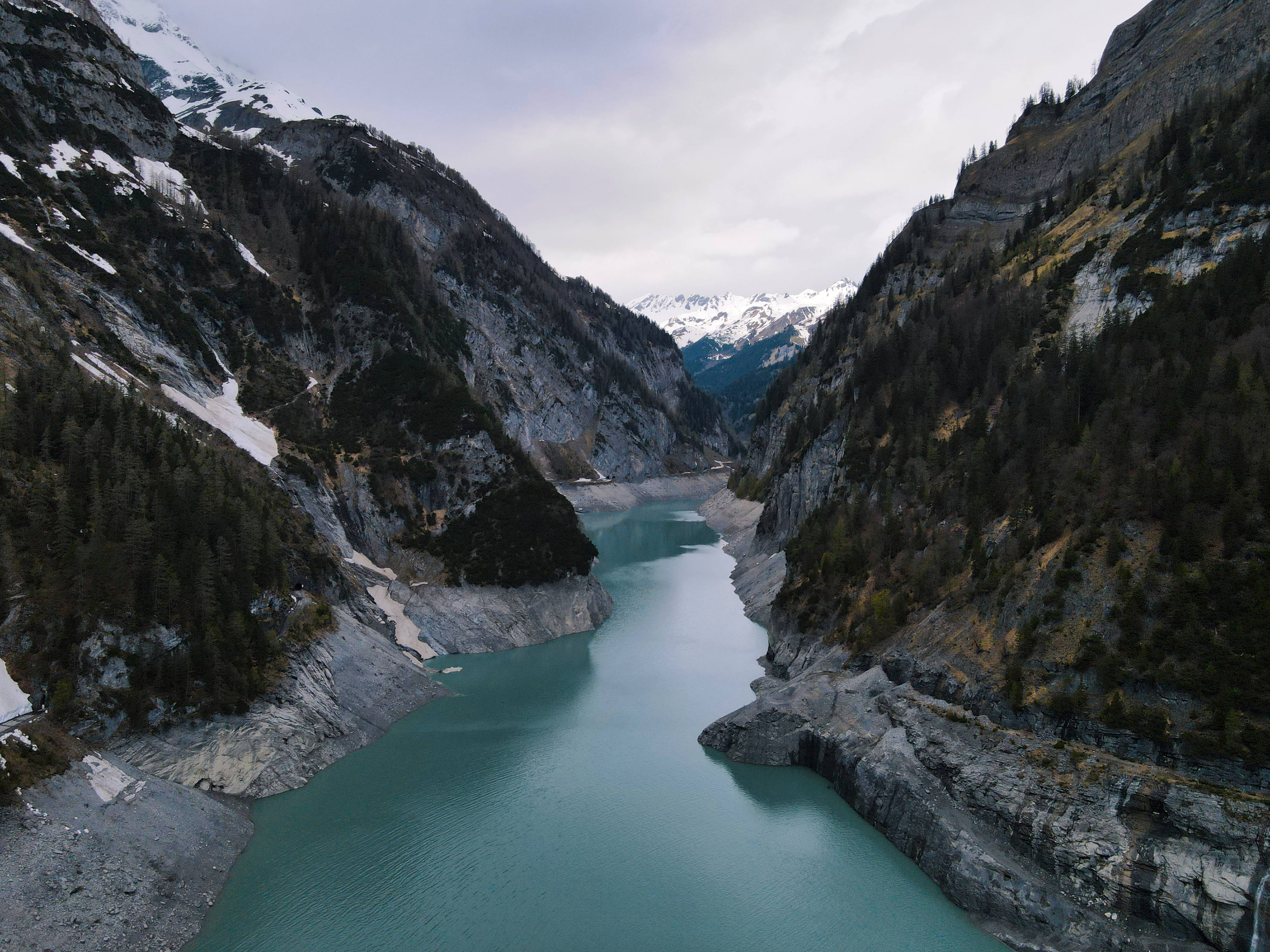 高山湖泊地貌 壁紙 — 俯瞰視角，一個藍綠色冰川湖坐落於積雪覆蓋的山脈之間，天空多雲。