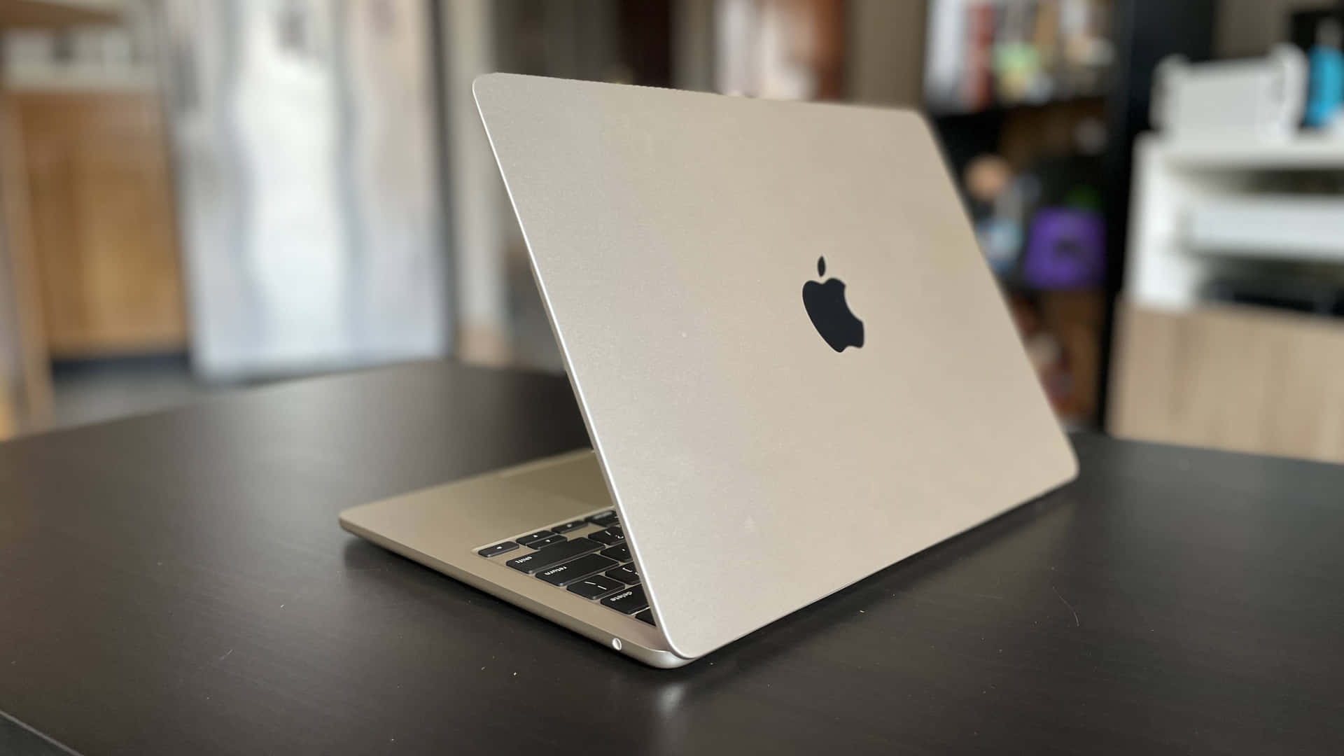 高性能 Apple MacBook 壁紙 — 一部銀色 MacBook 手提電腦打開放在深色木桌上，處於柔和光線的室內環境。